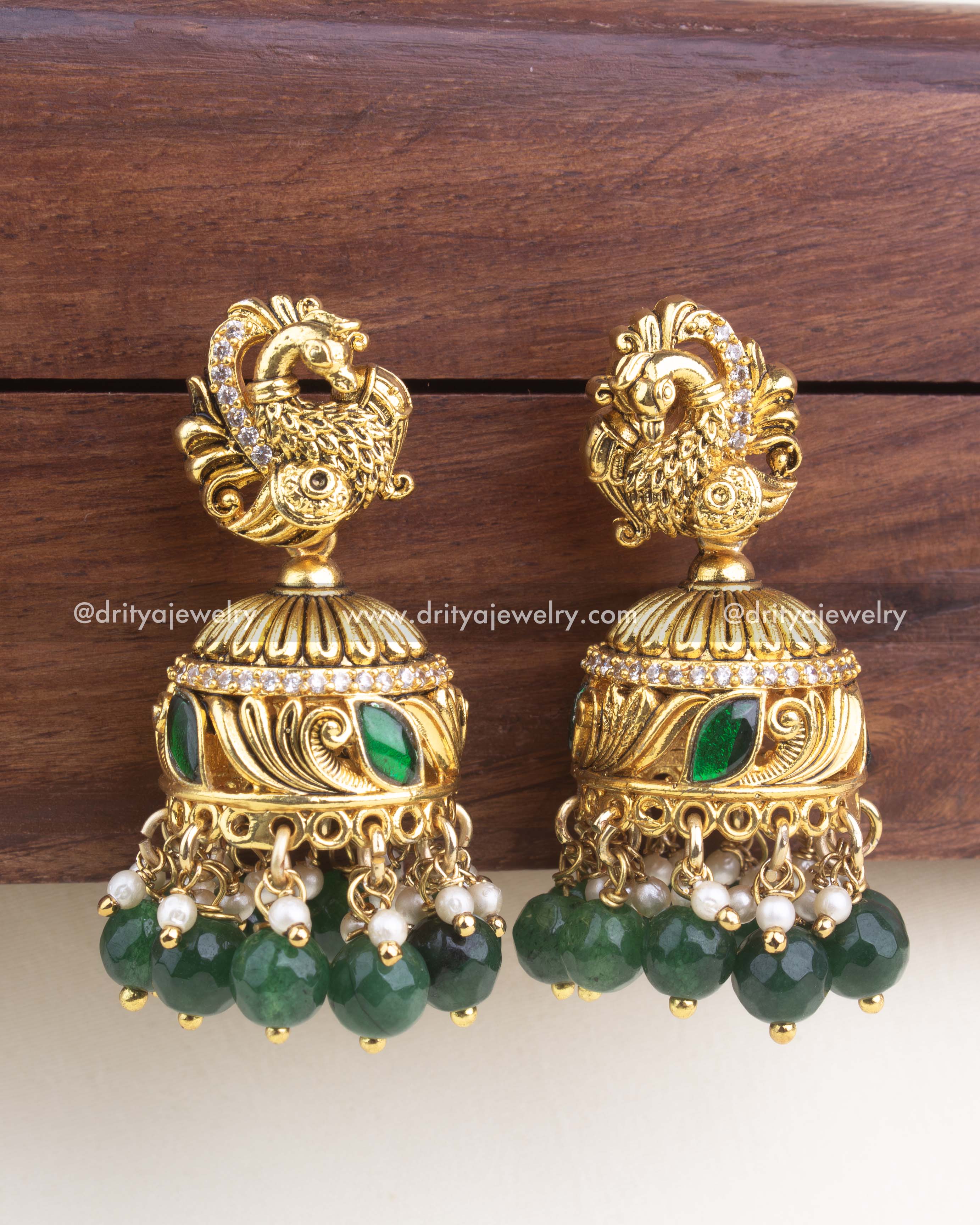 Gold-plated kemp jadau jhumka with peacock top, green enamel detailing, and emerald green bead hangings.