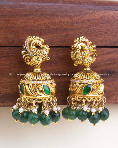 Gold-plated kemp jadau jhumka with peacock top, green enamel detailing, and emerald green bead hangings.