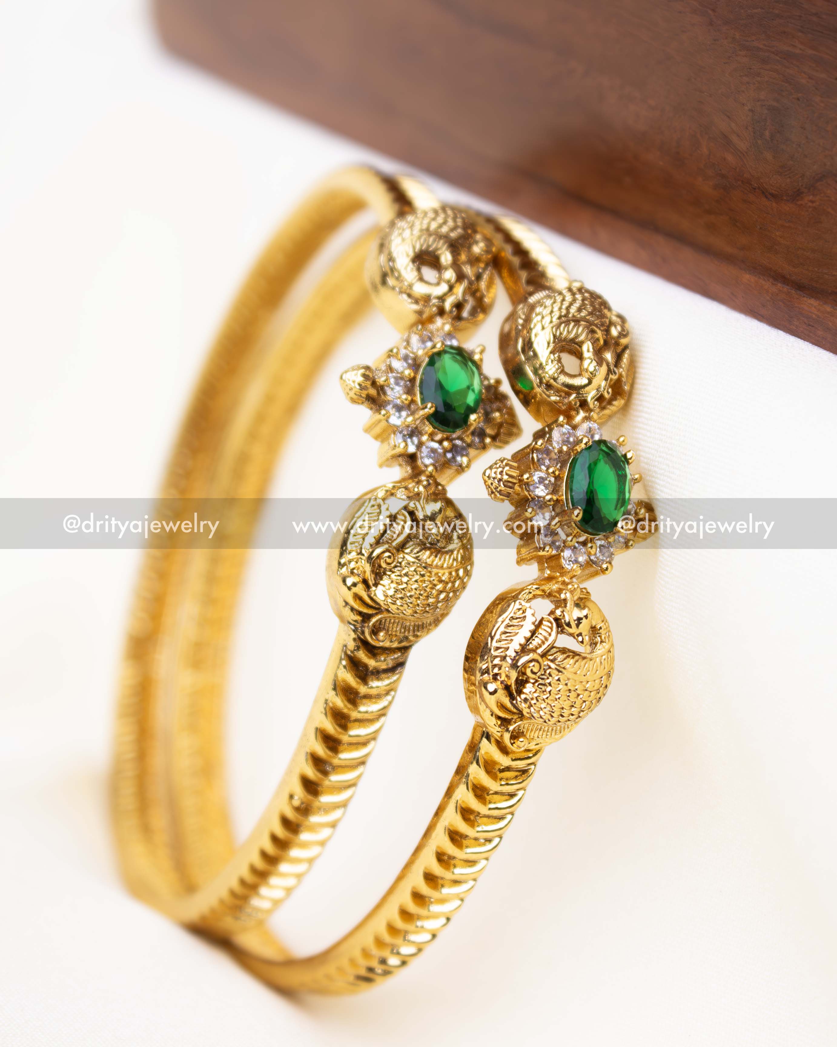 Gold-finished bangle pair with emerald green CZ stones and peacock motif.