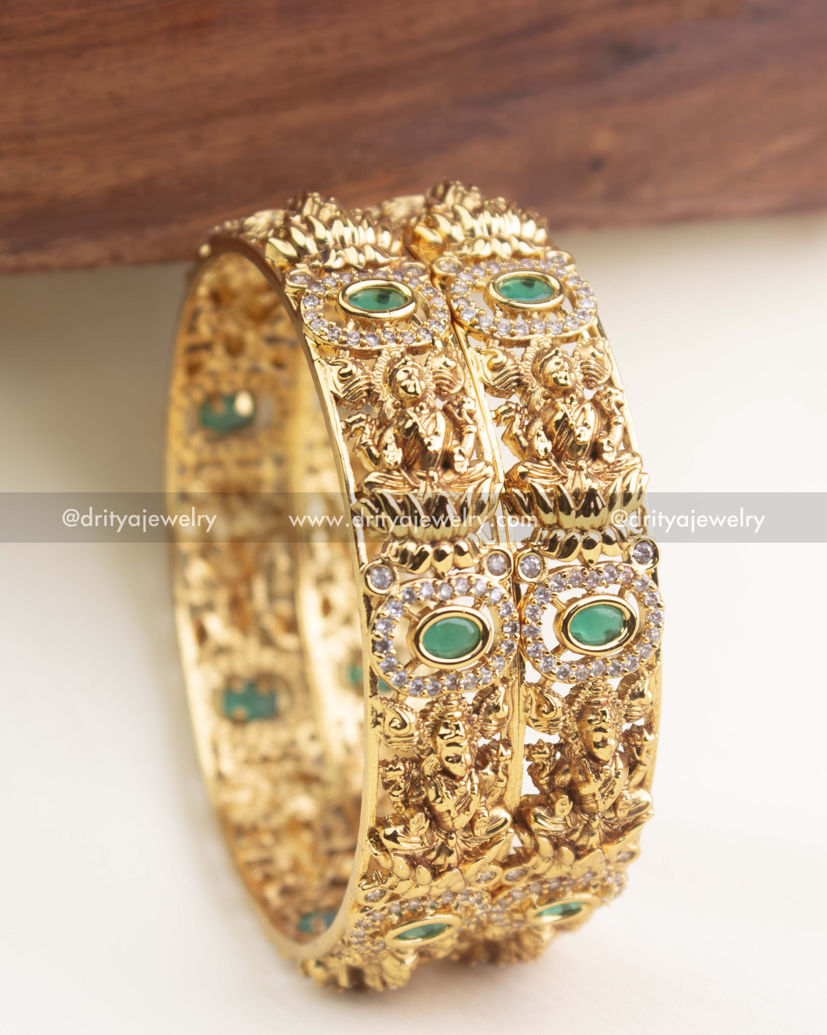 Gold temple bangles with intricate goddess motifs and oval emerald green stones surrounded by AD detailing