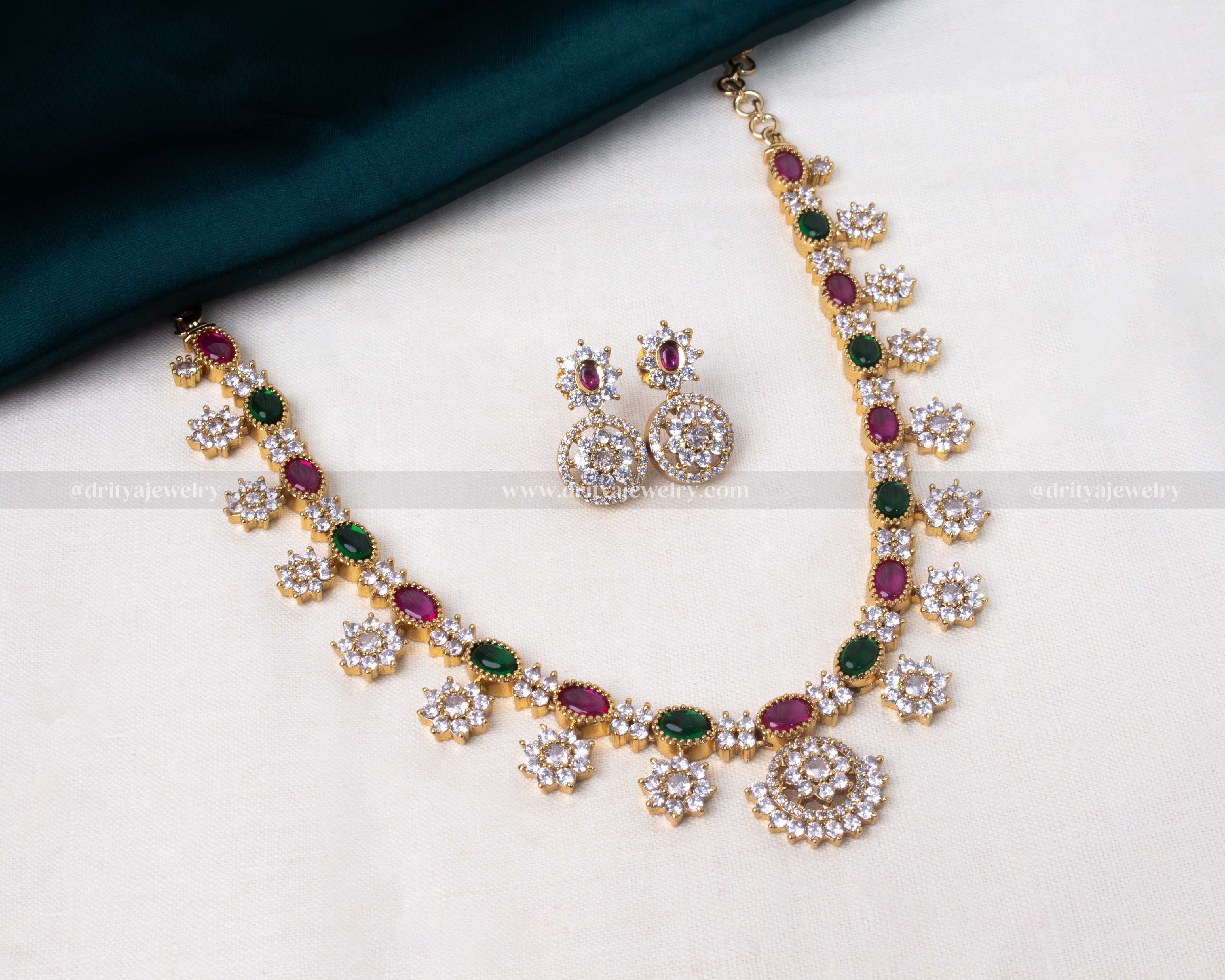 Elegant floral necklace set featuring green and pink stones with floral motifs in white stones, on a golden base.