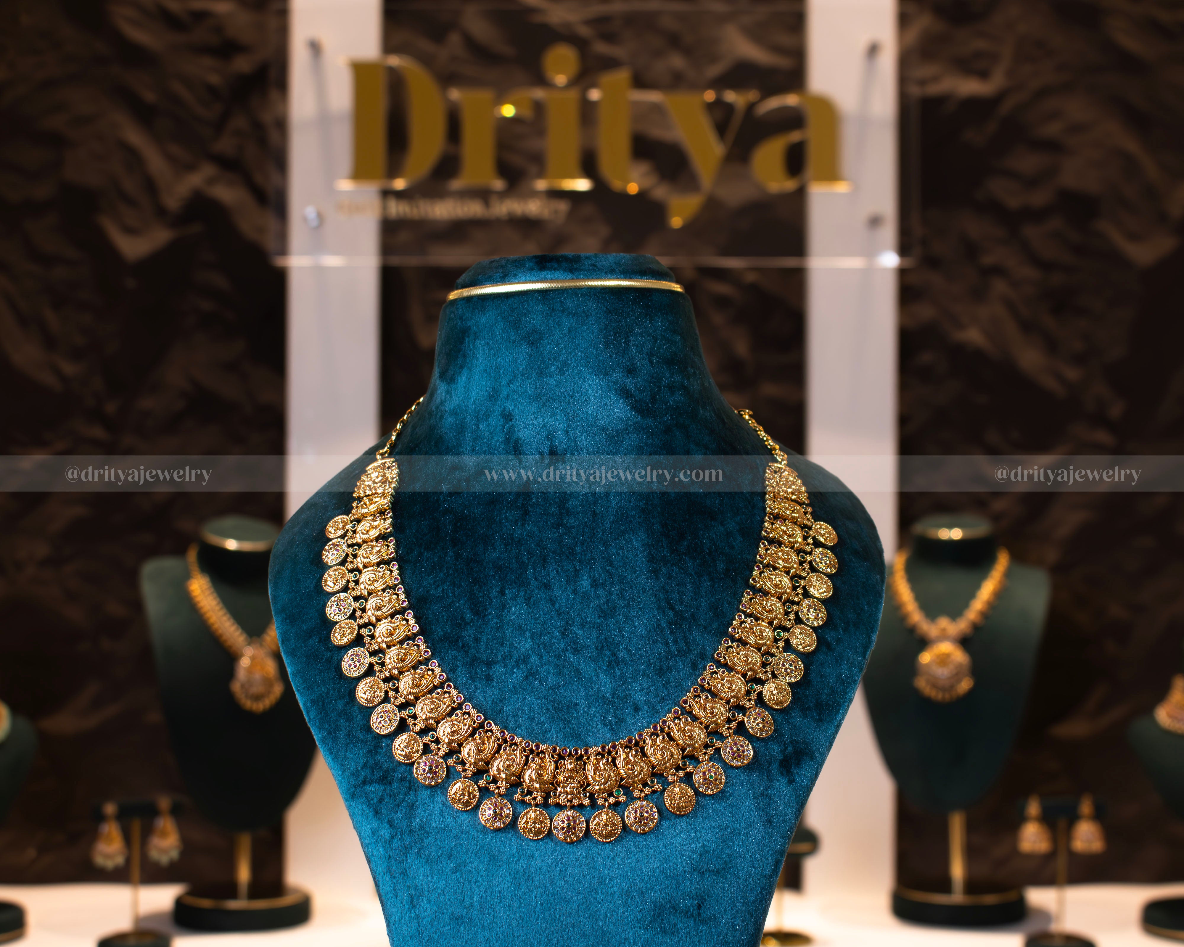 Front view of Dritya Jewelry’s Temple Coin Necklace set, showcasing intricate Lakshmi coins in an antique gold finish with ruby and emerald detailing.