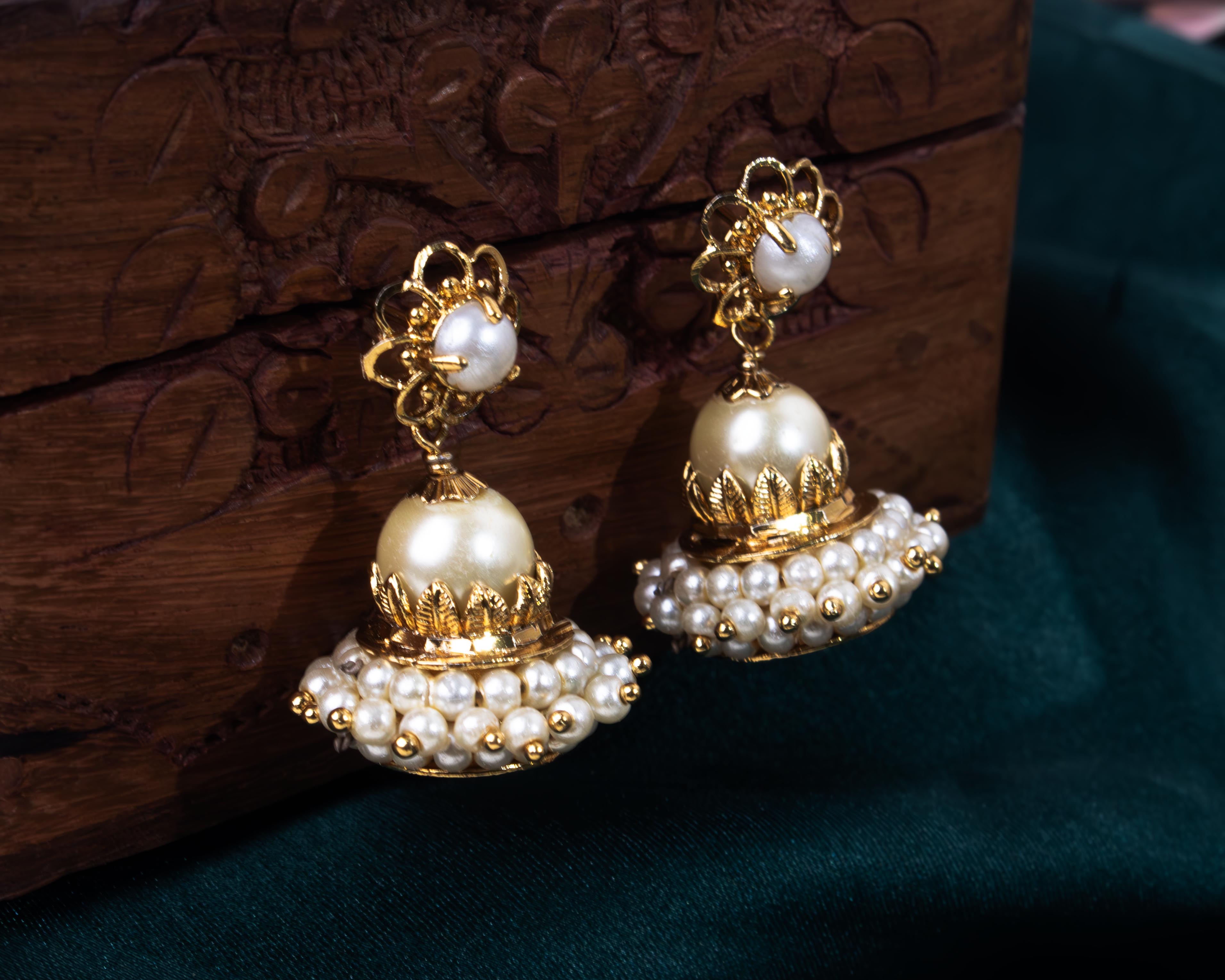 Elegant pearl jhumkas with a detachable feature against a rich wooden background, showcasing versatility.