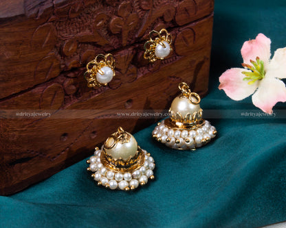 Elegant pearl jhumkas with a detachable feature against a rich wooden background, showcasing versatility.