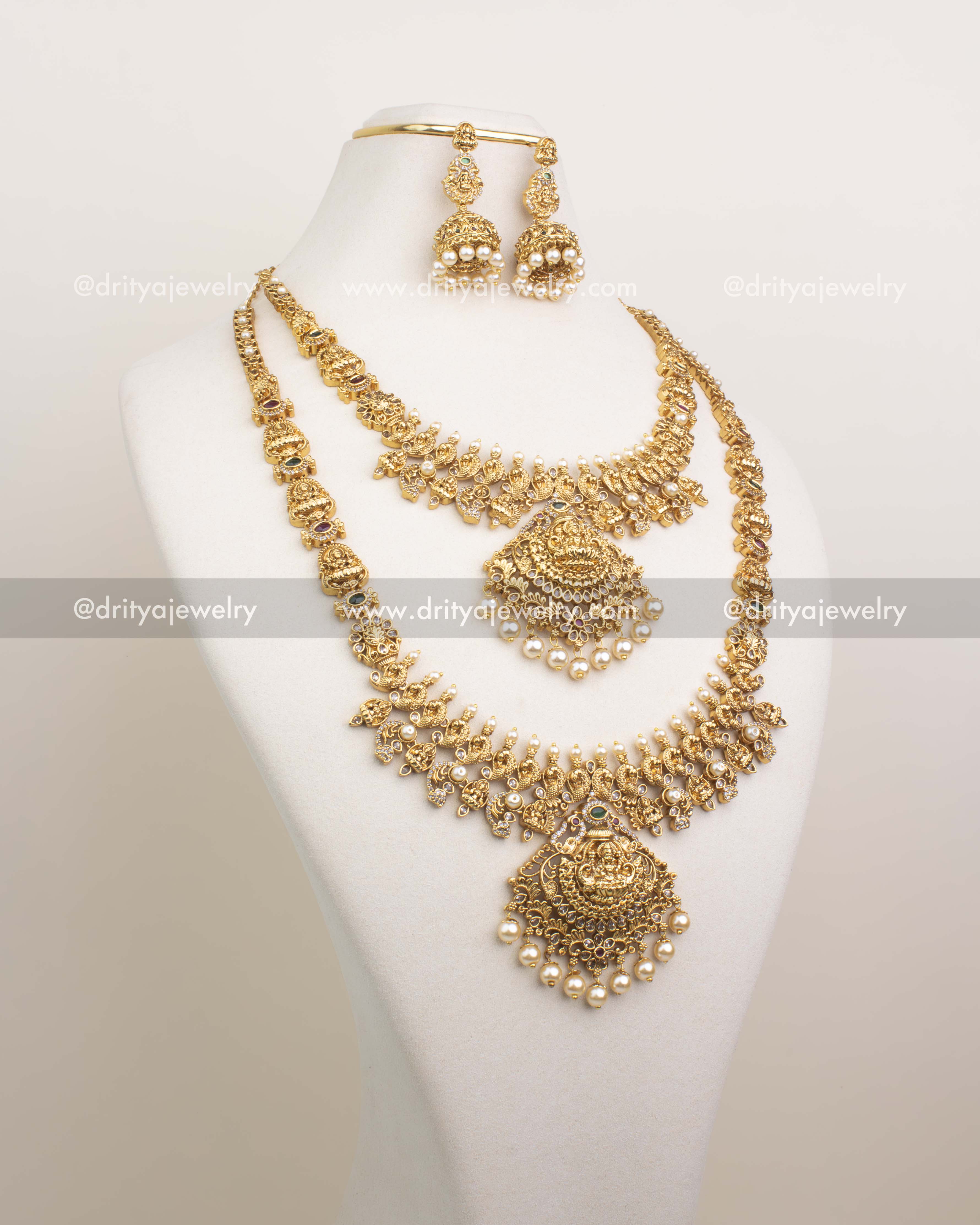 Premium four-piece temple jewelry set with Lakshmi Devi motifs, featuring long haram, short necklace, jhumkas, and maang tikka on display bust.
