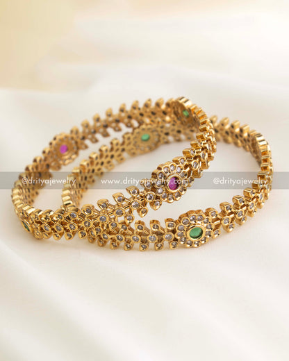 Elegant gold-finished imitation bangles featuring alternating ruby red and emerald green center stones surrounded by floral CZ patterns from Dritya Jewelry.