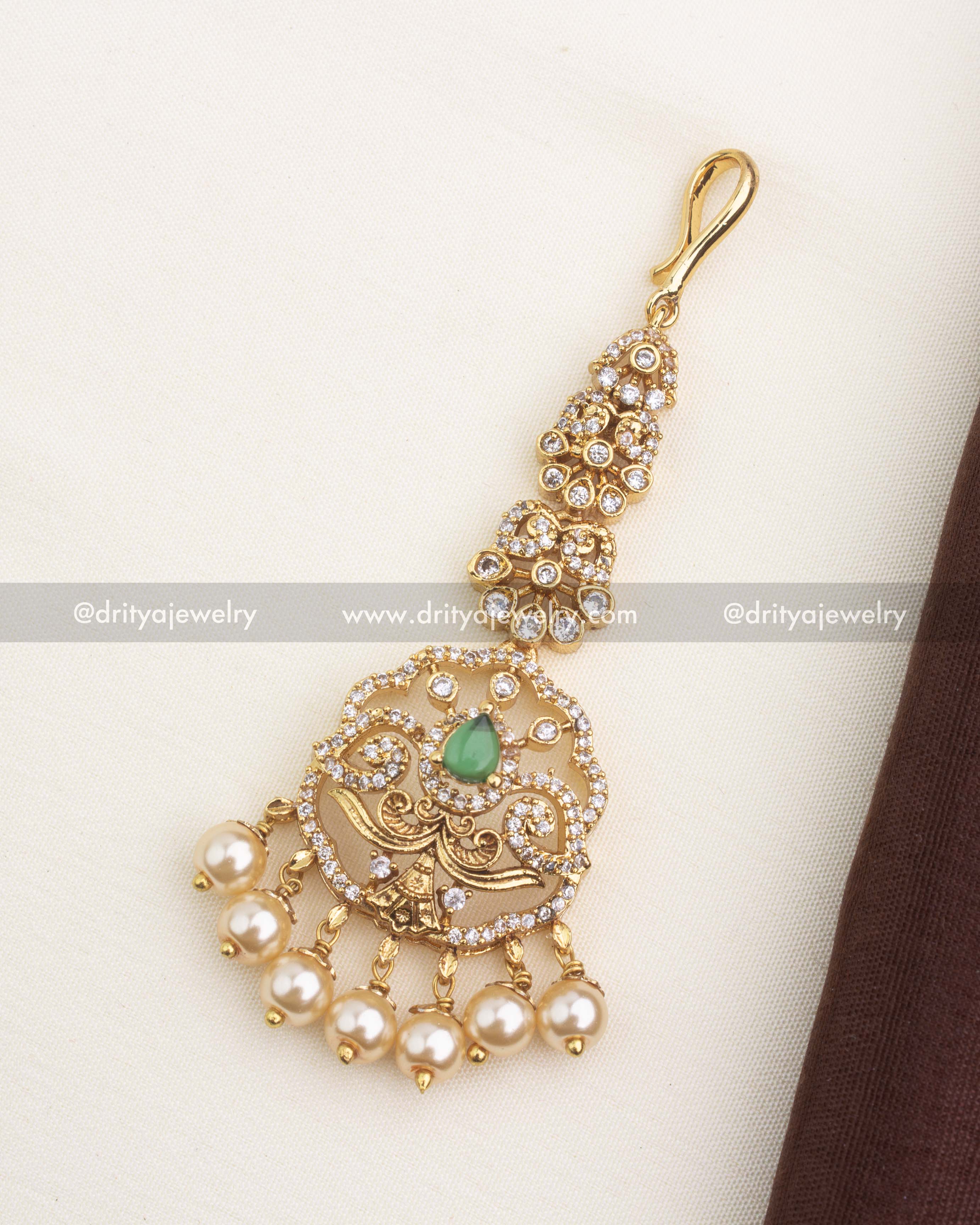 Gold replica maang tikka with emerald green stone centerpiece, CZ embellishments, and pearl drop detailing.