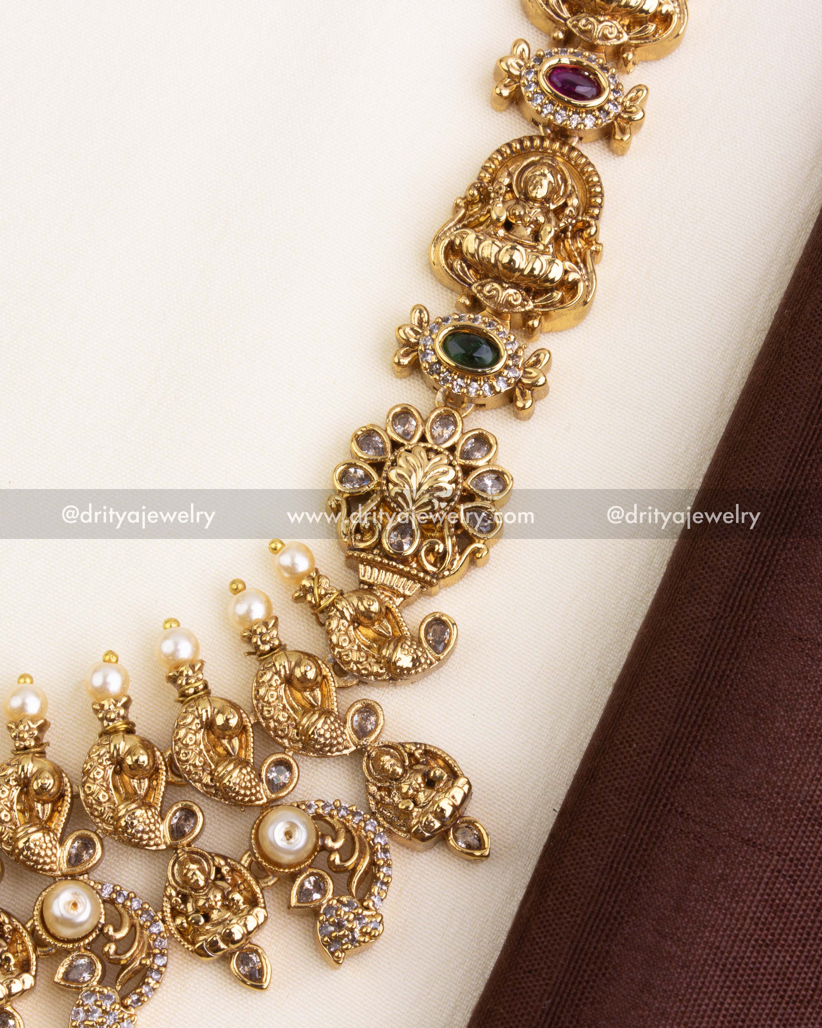 Detailed view of Lakshmi Devi idols, ruby-emerald stones, and floral links on gold-plated long temple haram.