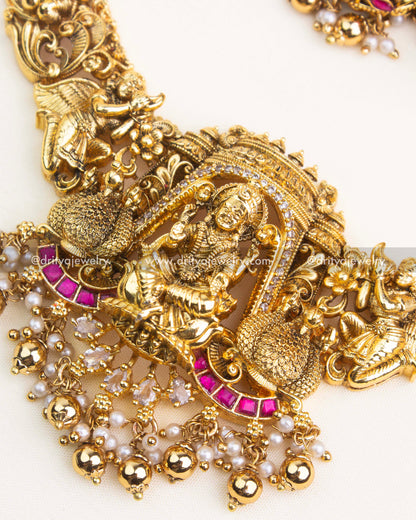Close-up of temple necklace showing detailed Lakshmi pendant, peacock motifs, pearl hangings, and kemp stones.