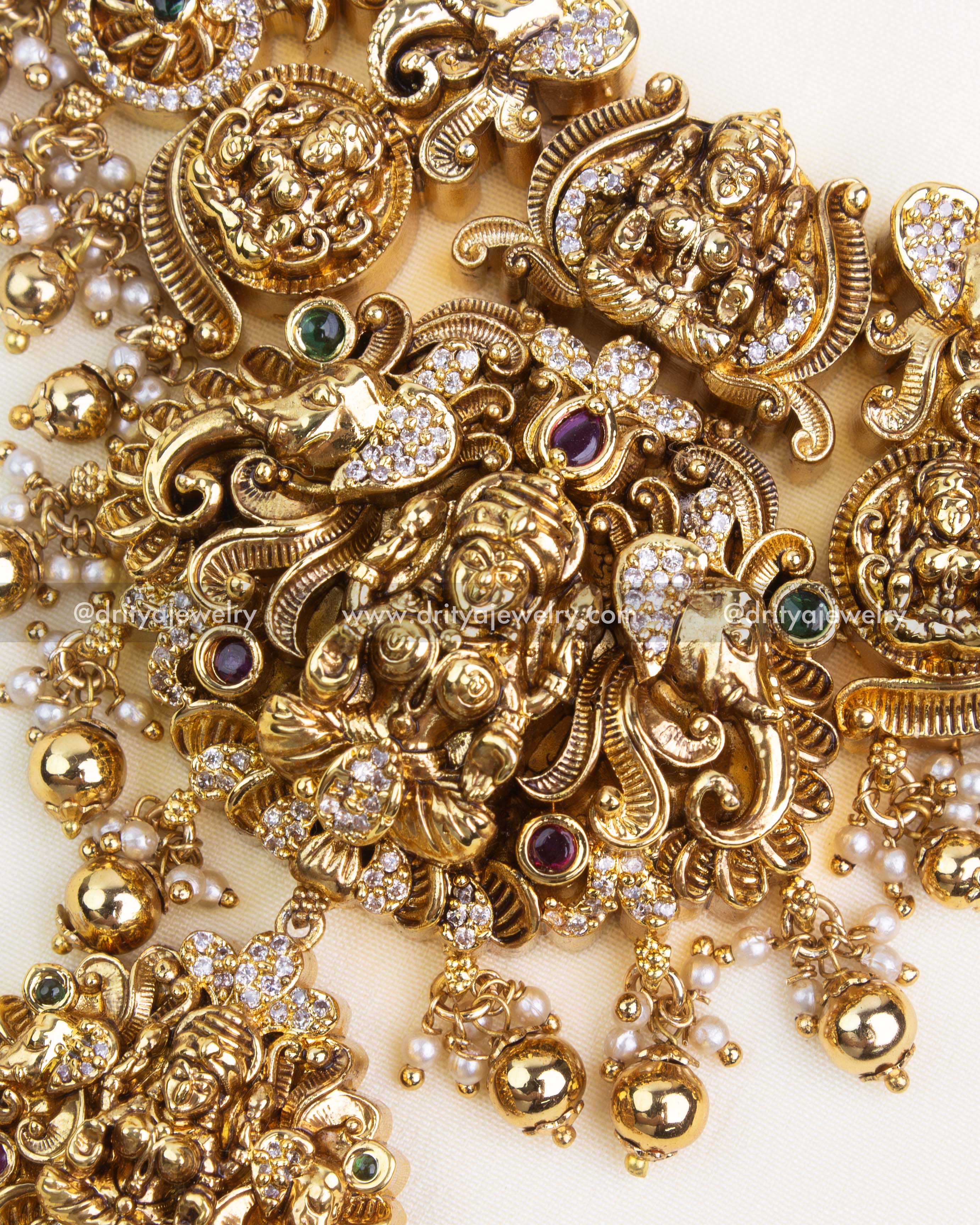 Central Lakshmi panel with ornate scrolls, AD stonework, and dangling ghungroo drops for a traditional bridal look.