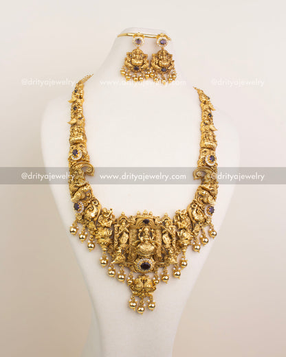 Side-angle view of Nakshi bridal long necklace set featuring Lakshmi Devi motif, purple stones, white CZ detailing, and traditional craftsmanship