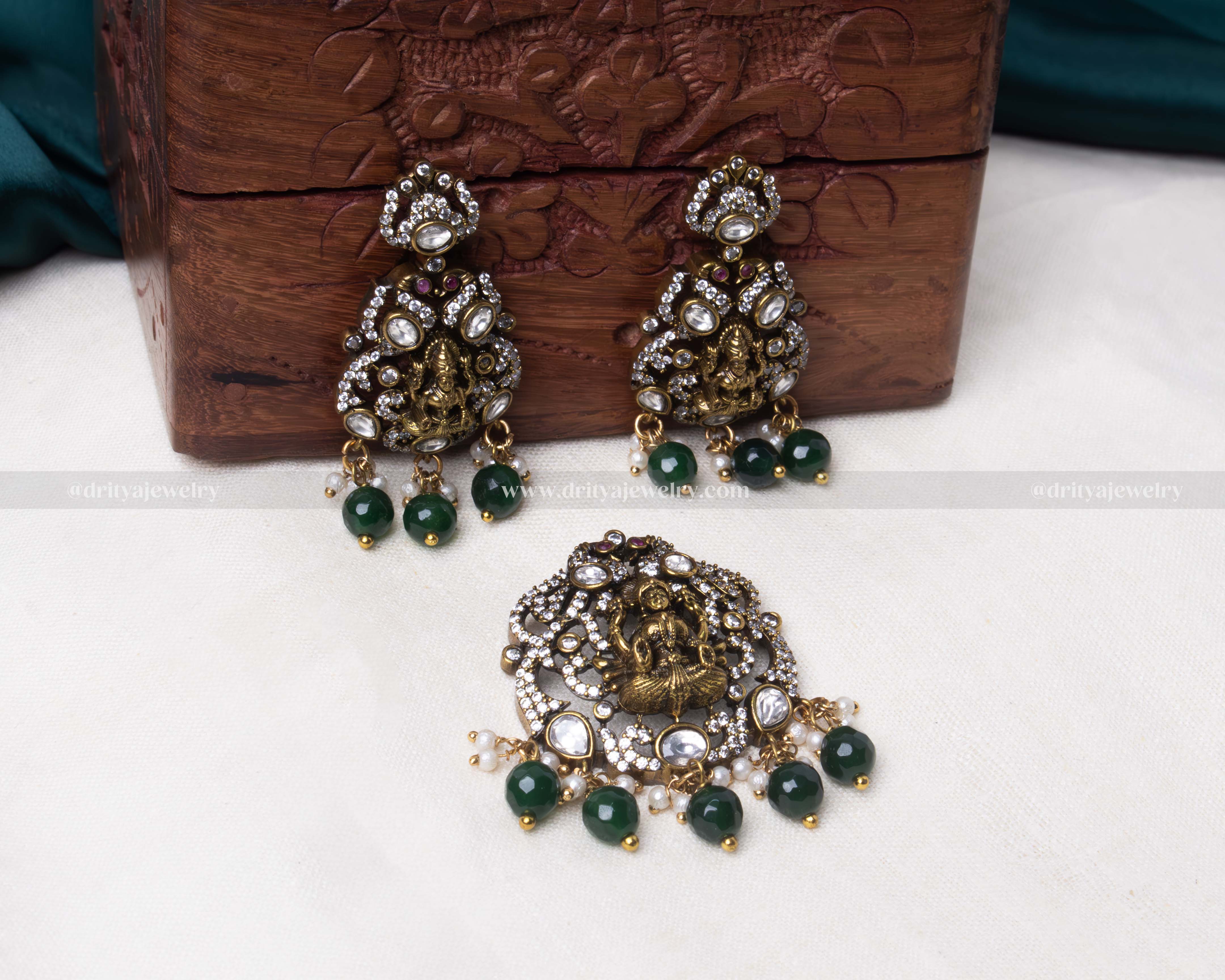 Antique gold pendant set featuring Lakshmi Devi, adorned with Kundan stones, green beads, and pearls, with matching earrings.