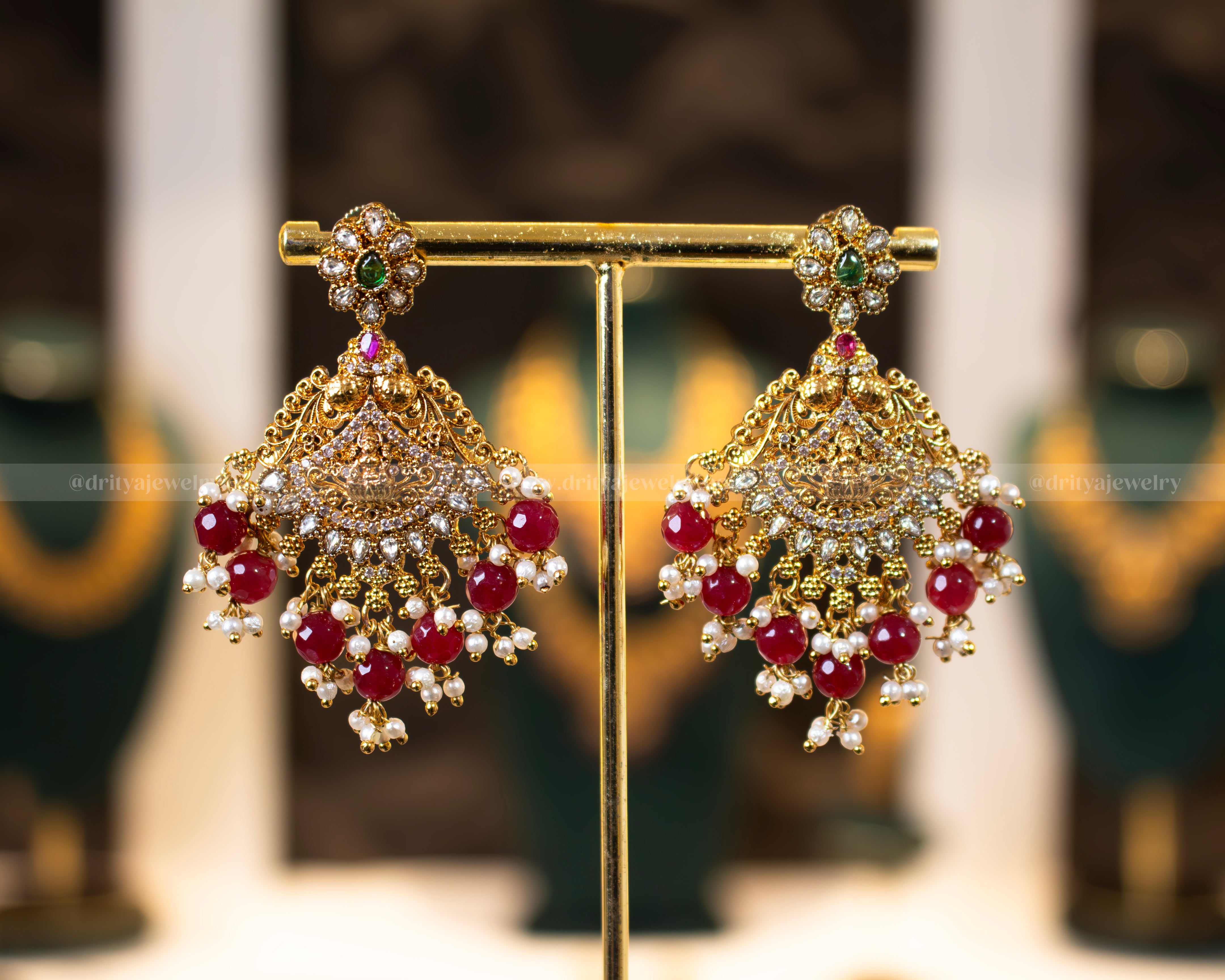 Matching earrings of Dritya Jewelry's Lakshmi Devi Temple Necklace Set with intricate gold-plated design and ruby-like bead embellishments.