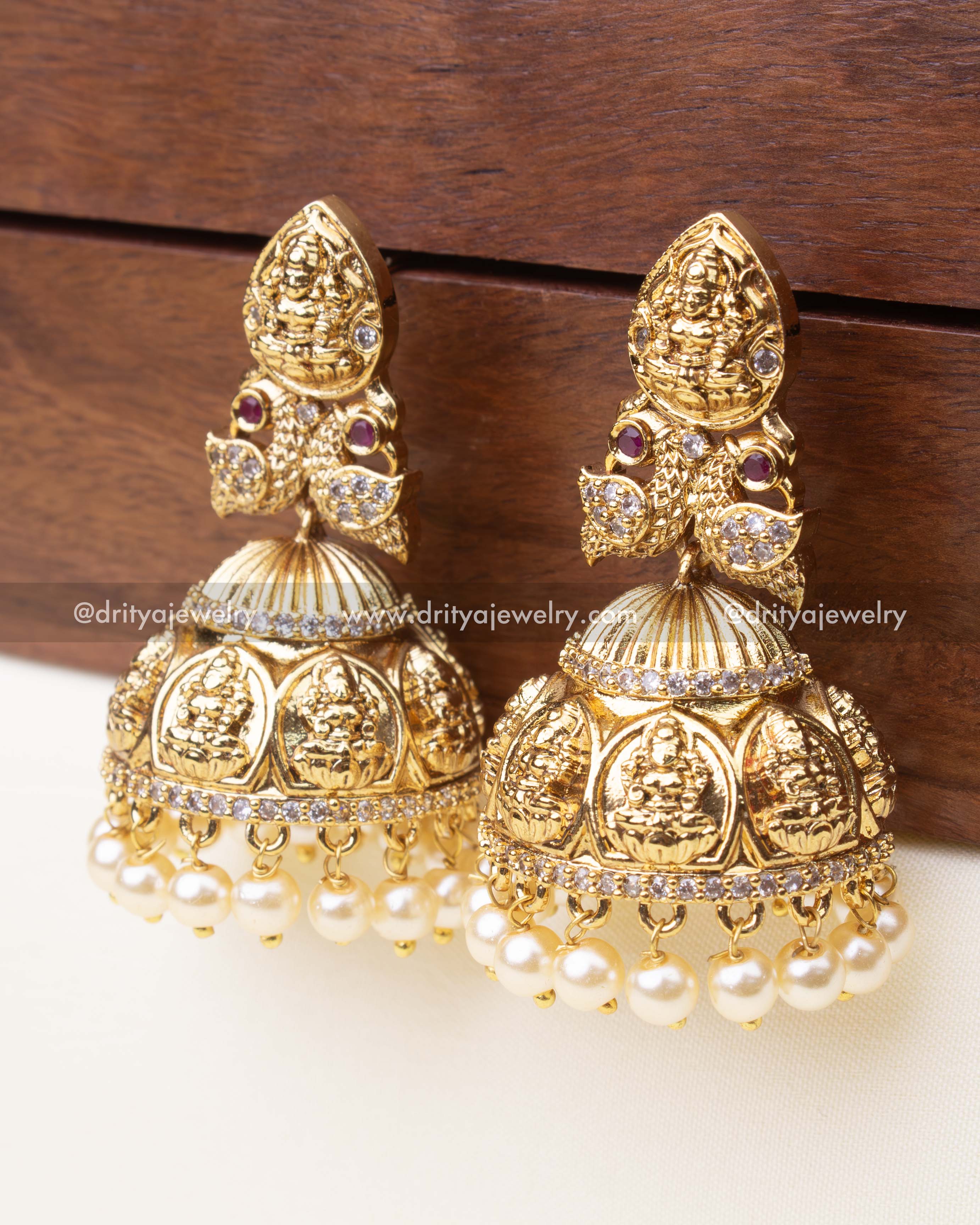Side view showcasing Lakshmi motifs, dome structure, and pearl fringe on gold-plated jhumka earrings.