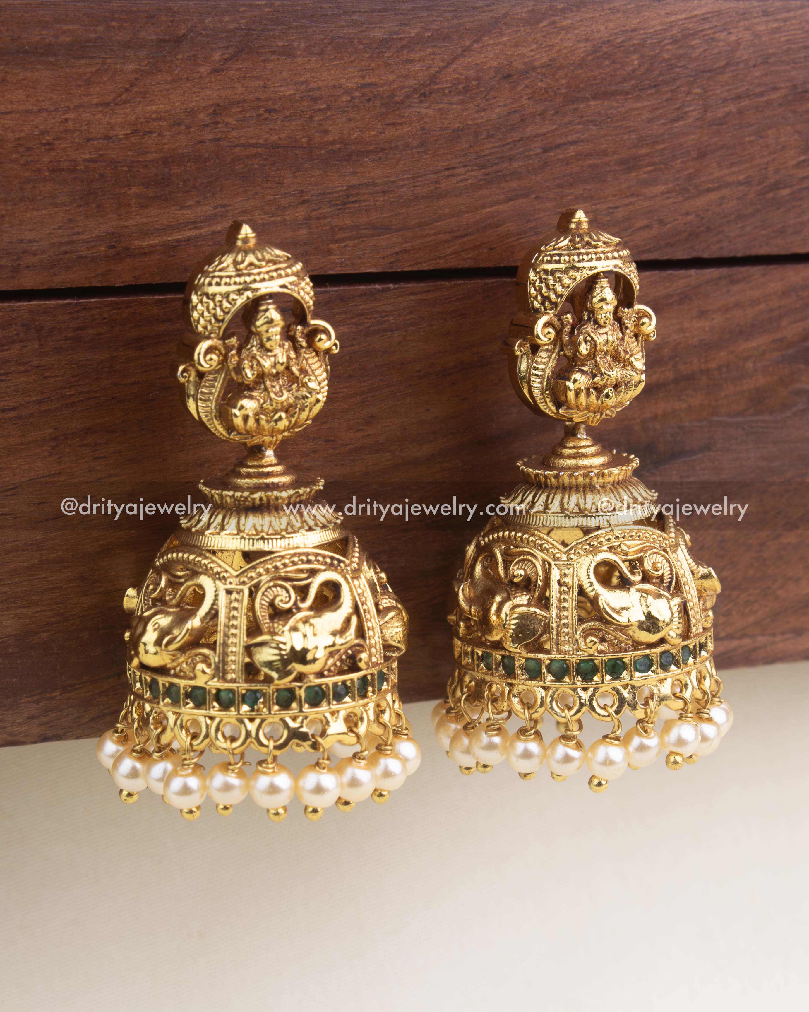 Close-up of premium temple jhumka showing Goddess Lakshmi, nakshi dome carving, green stones, and pearl embellishments.