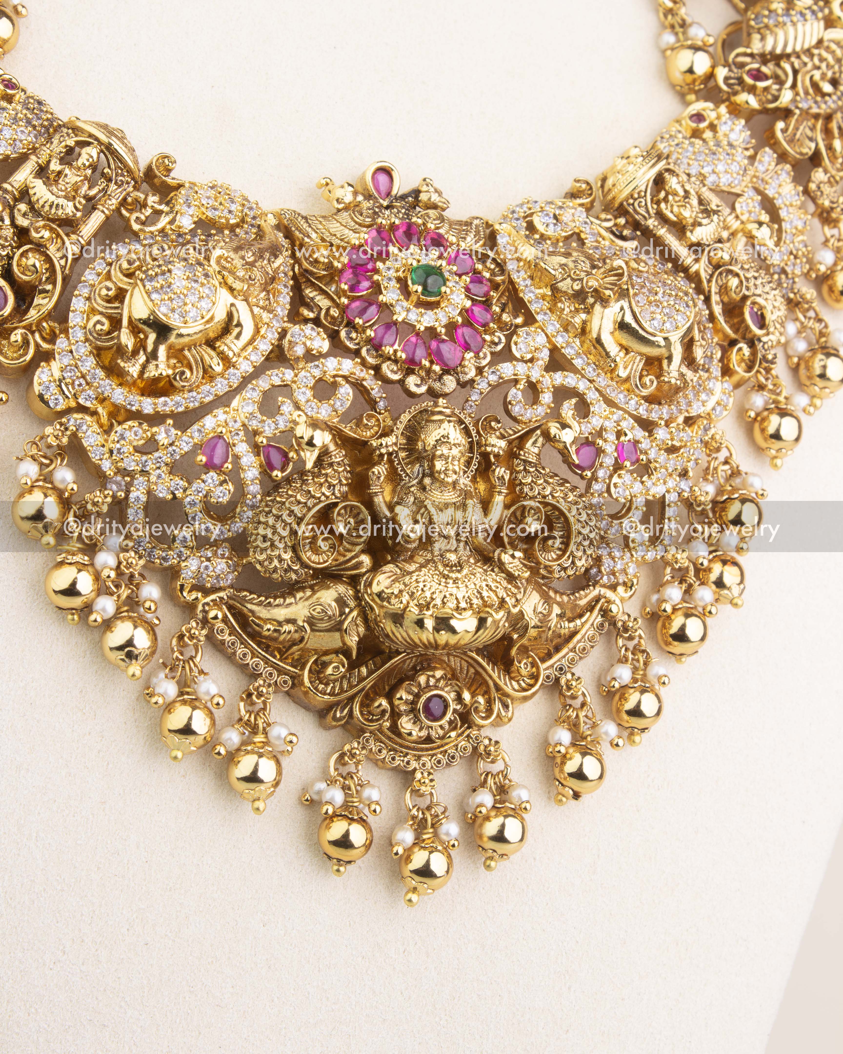 Close-up of temple-style long necklace with Lakshmi motif, ruby kemp stones, and golden bead drops.