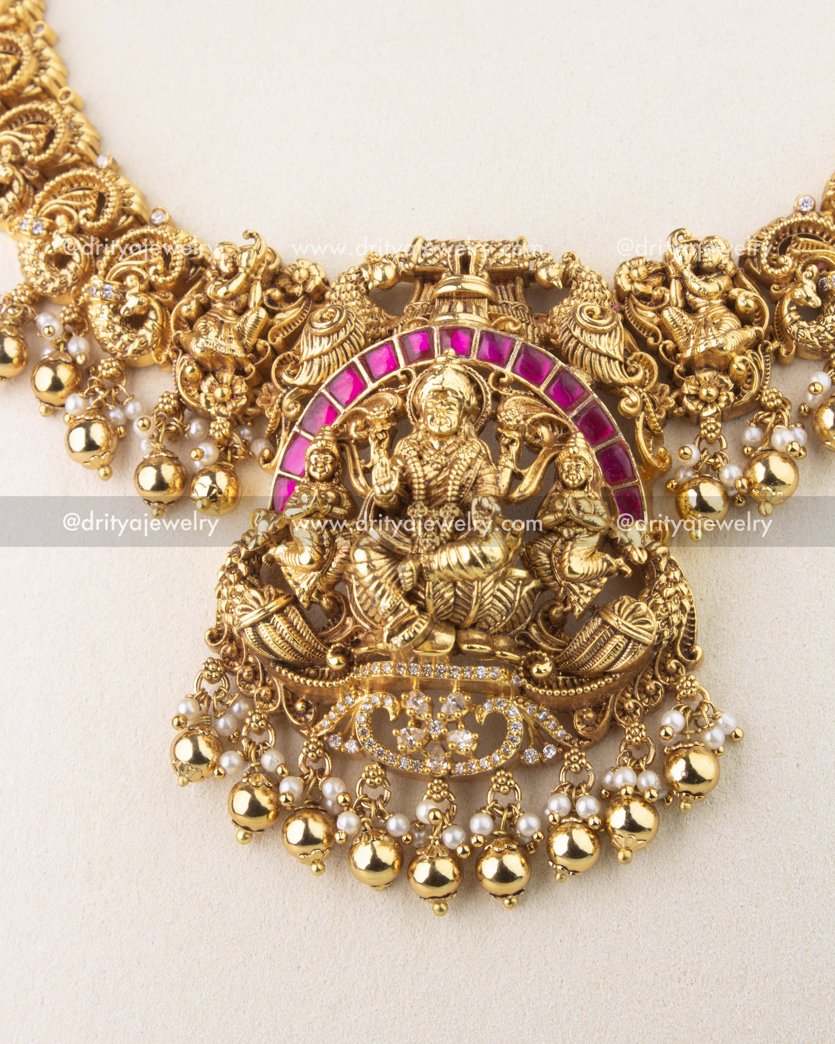 Detailed view of Lakshmi motif pendant with ruby kemp stones, peacock carvings, and pearl drops.