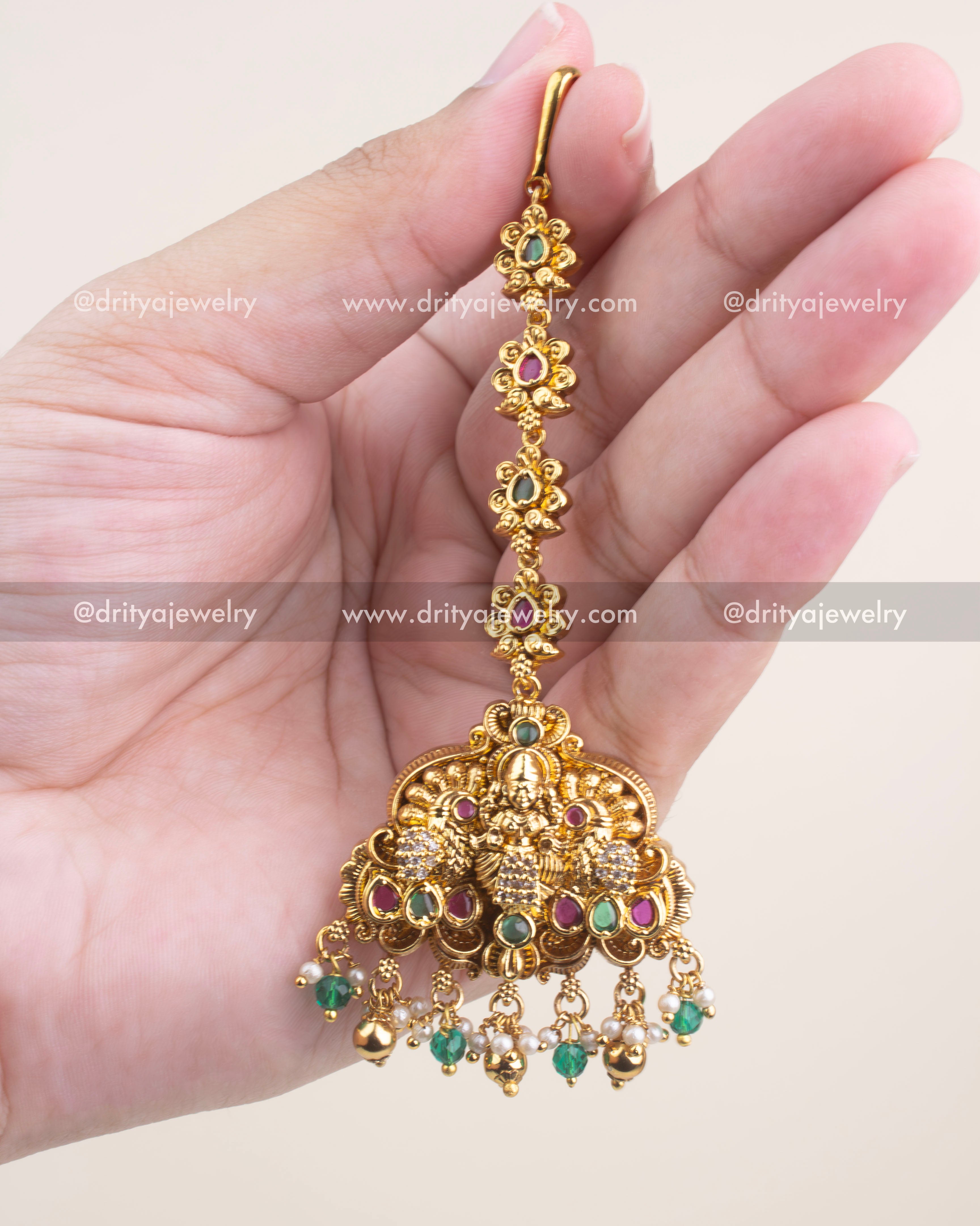 Temple-style maang tikka in antique gold with CZ stones and emerald green bead drops.