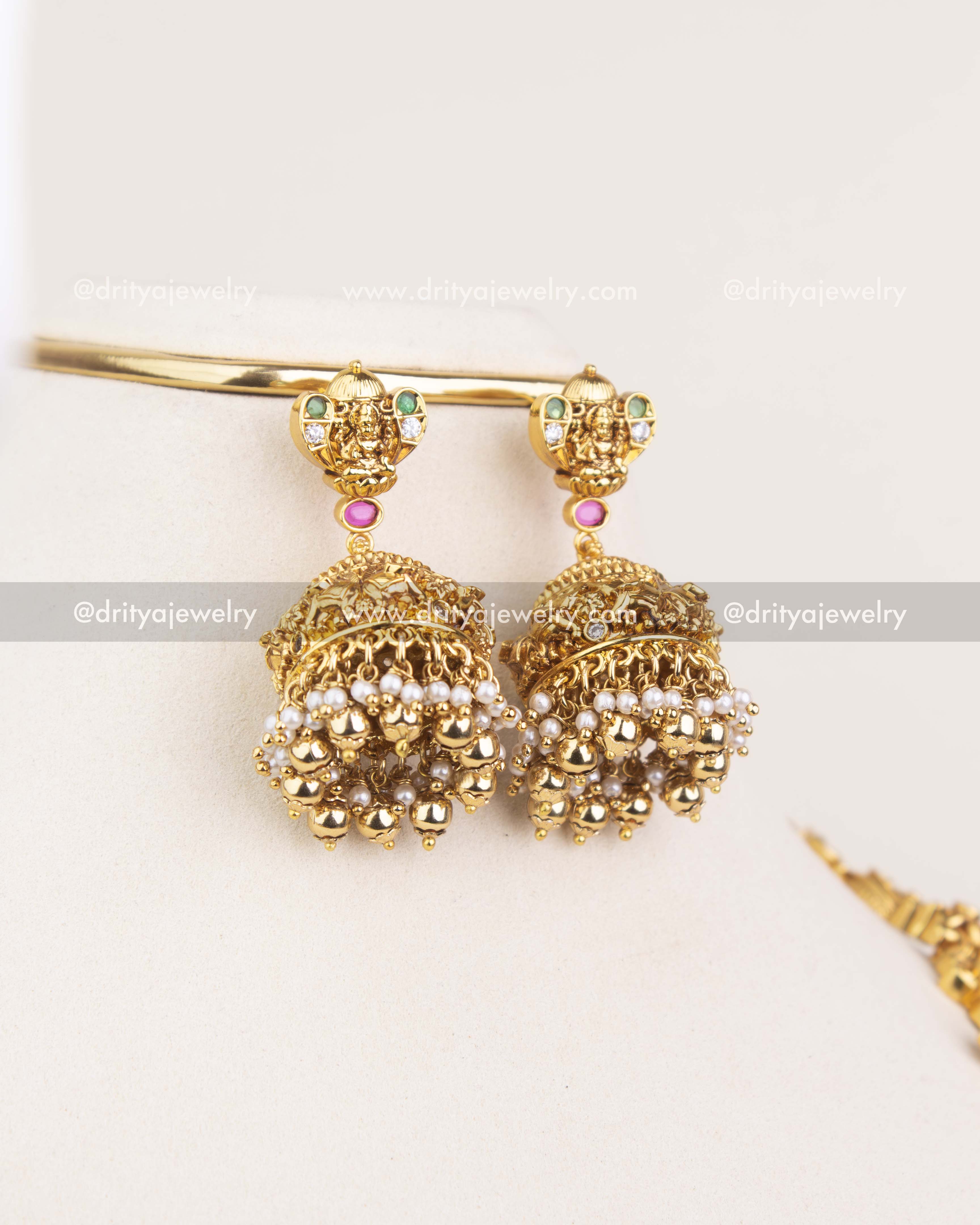 Temple-style bridal jhumka earrings with deity detailing, CZ stones, and pearl-gold drops.