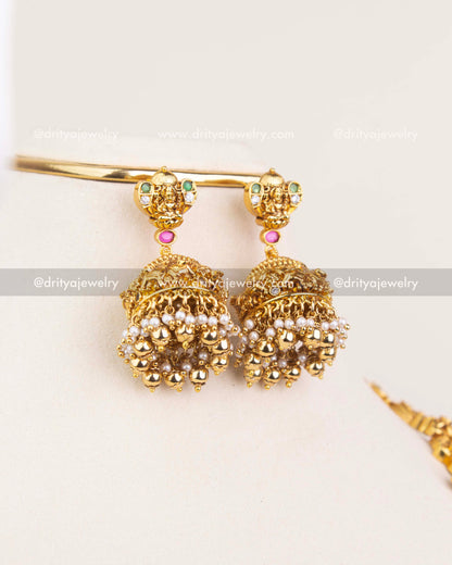 Temple-style bridal jhumka earrings with deity detailing, CZ stones, and pearl-gold drops.