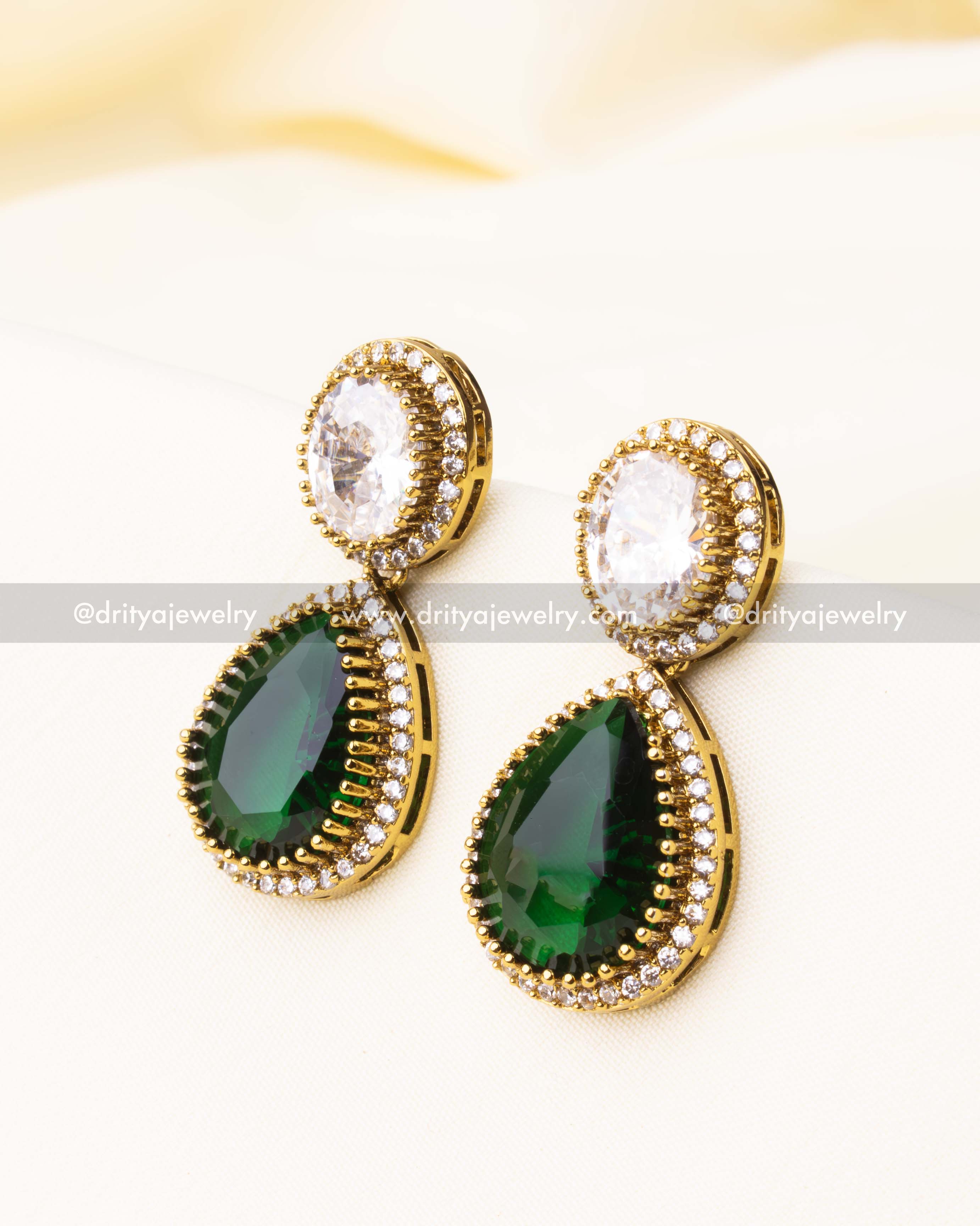 Close-up of drop earrings with green and white CZ stones in teardrop and oval shapes