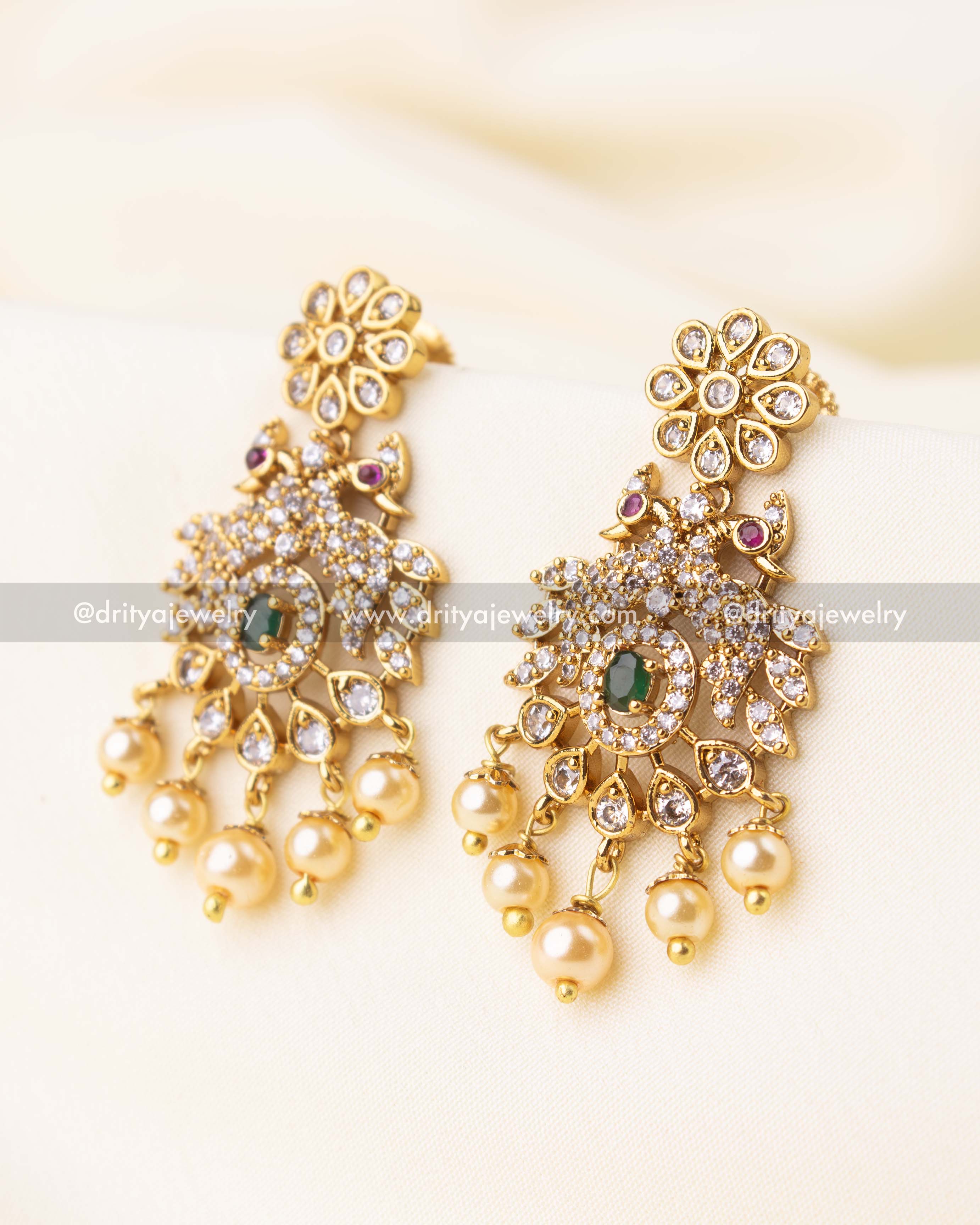 Coordinated earrings with floral top, green stones, peacock elements, and pearl drops.