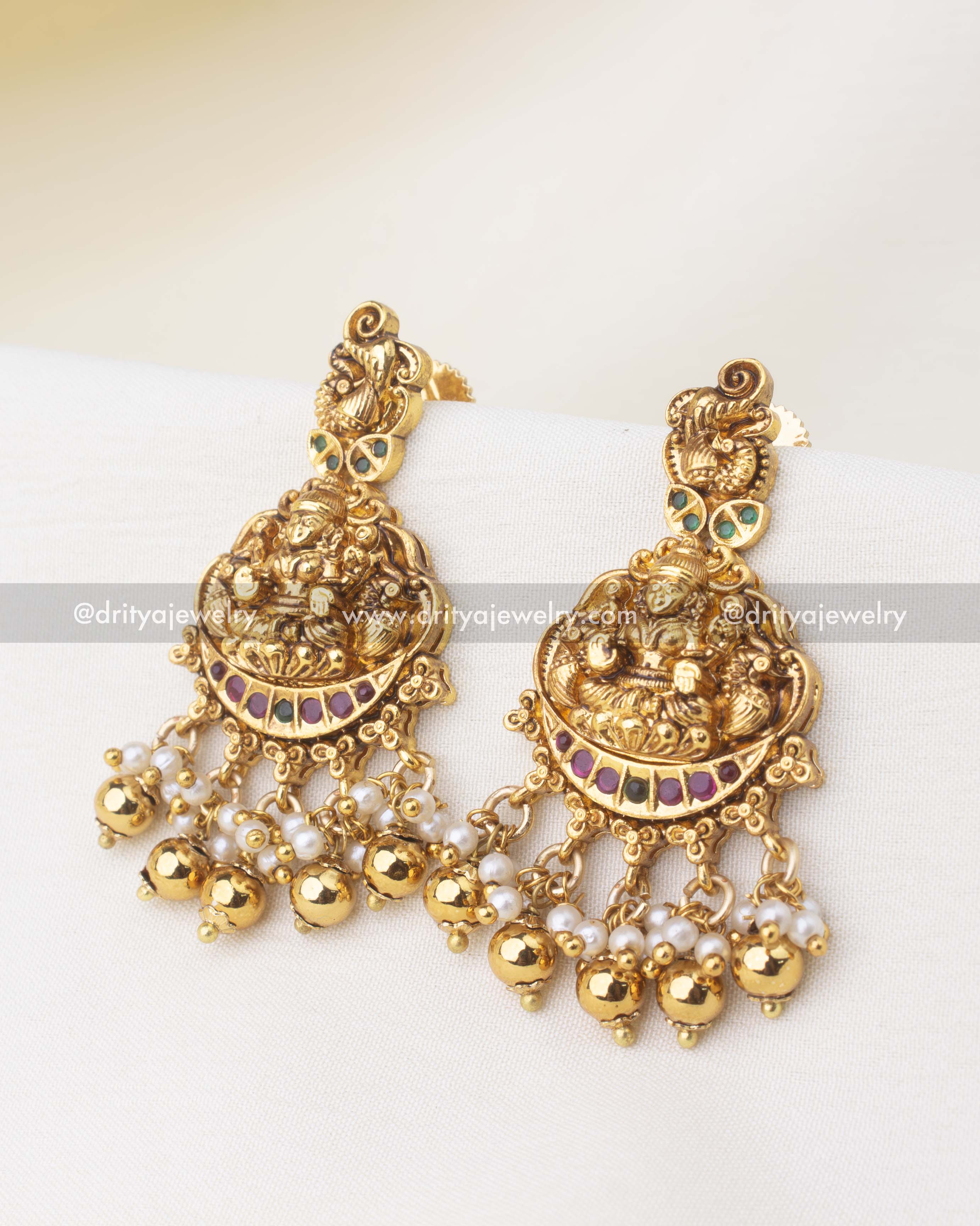 Antique gold jhumka-style earrings with Goddess motif, ruby-green highlights, and pearl drops.