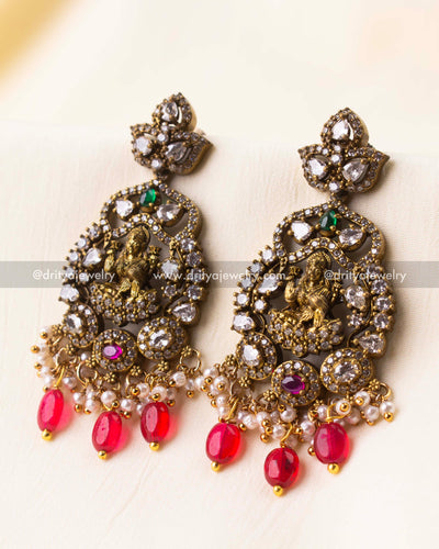 Temple-inspired earrings featuring a central deity motif, Victorian CZ work, pearls, and ruby-colored bead drops