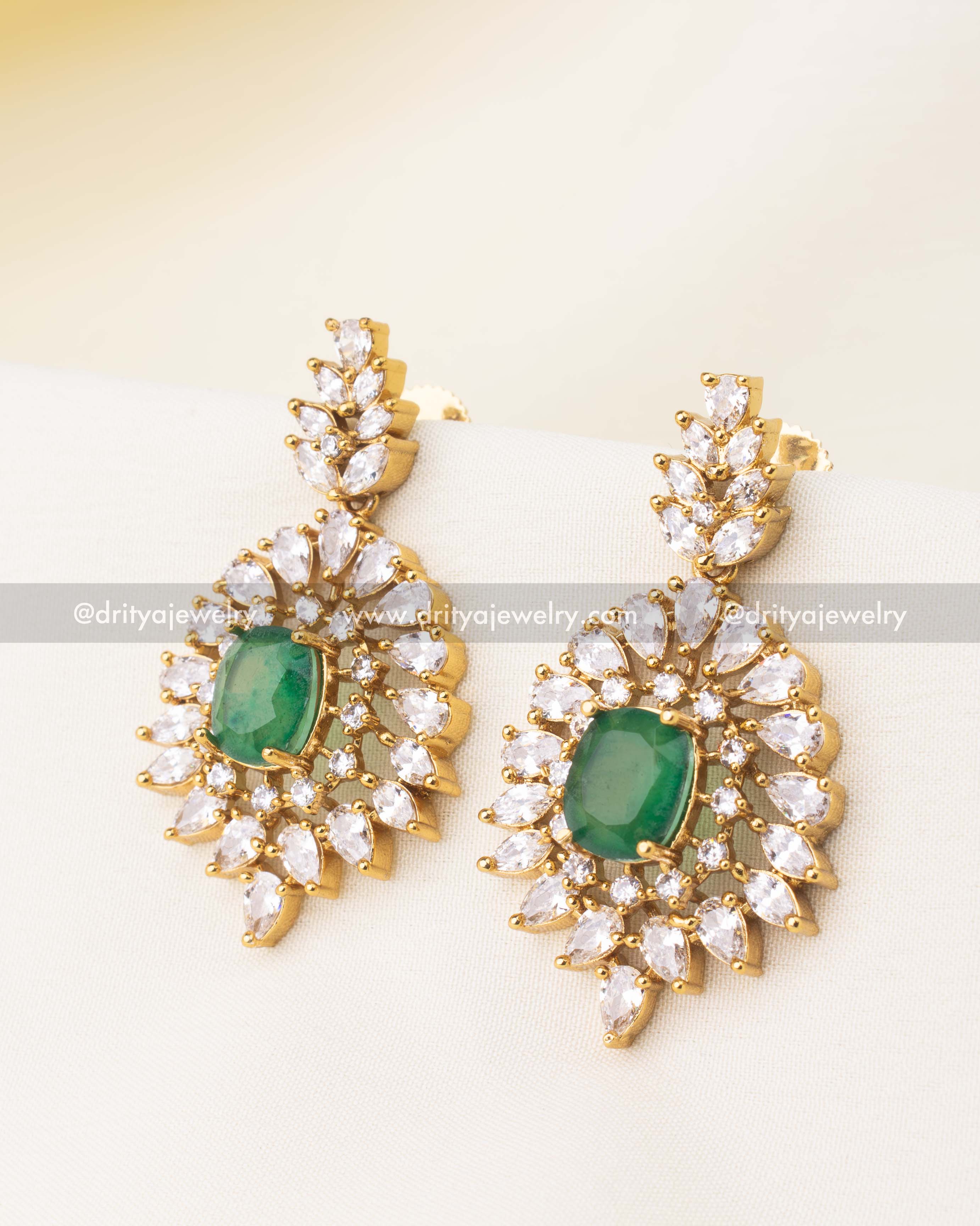 Drop earrings with emerald‑green center and layered CZ halo in a starburst design.