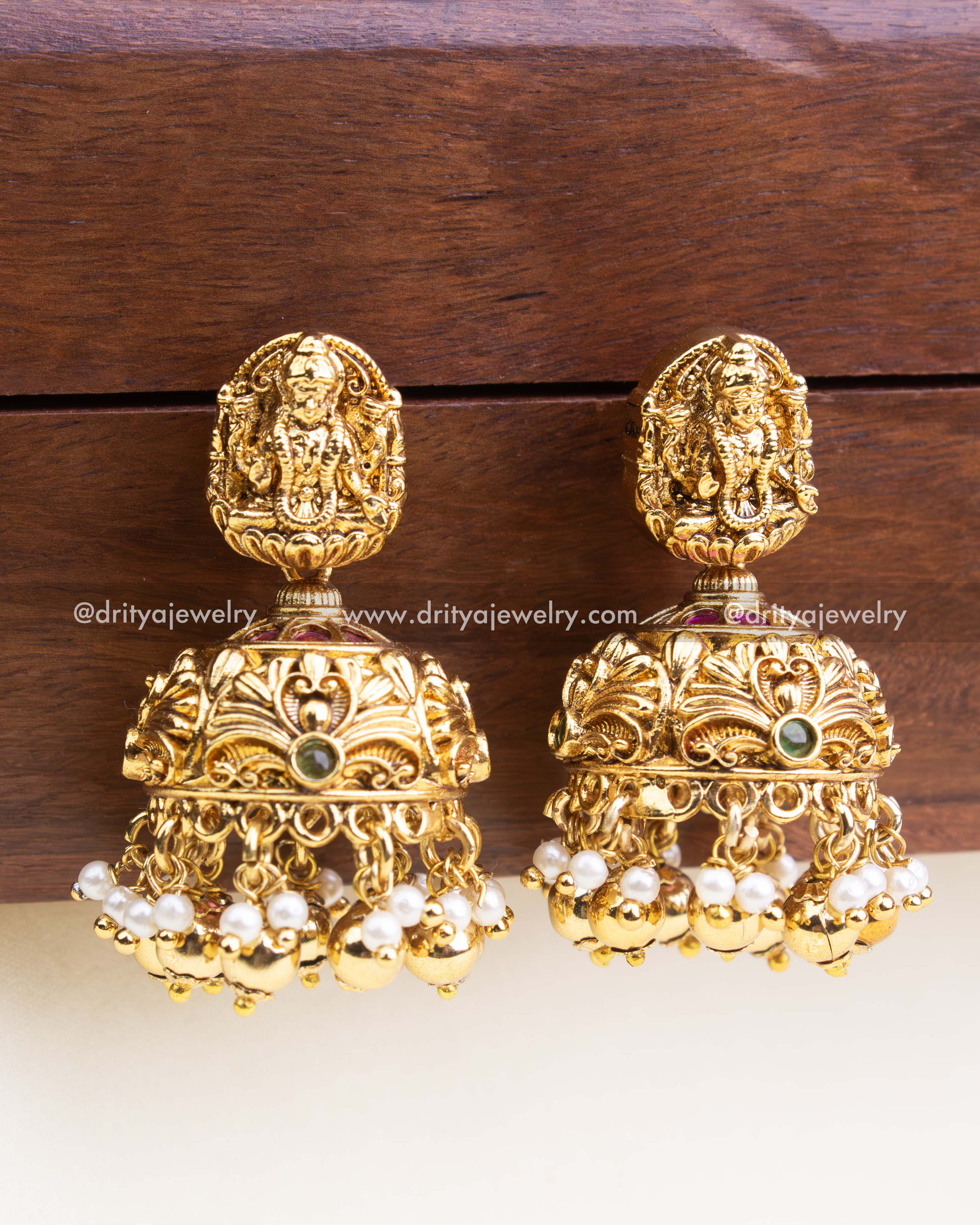 Dome-shaped jhumka earrings with Lakshmi motifs and pearl cluster hangings in antique finish.