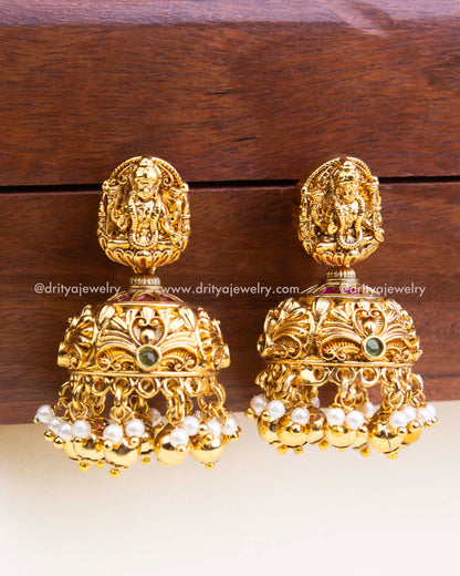 Dome-shaped jhumka earrings with Lakshmi motifs and pearl cluster hangings in antique finish.