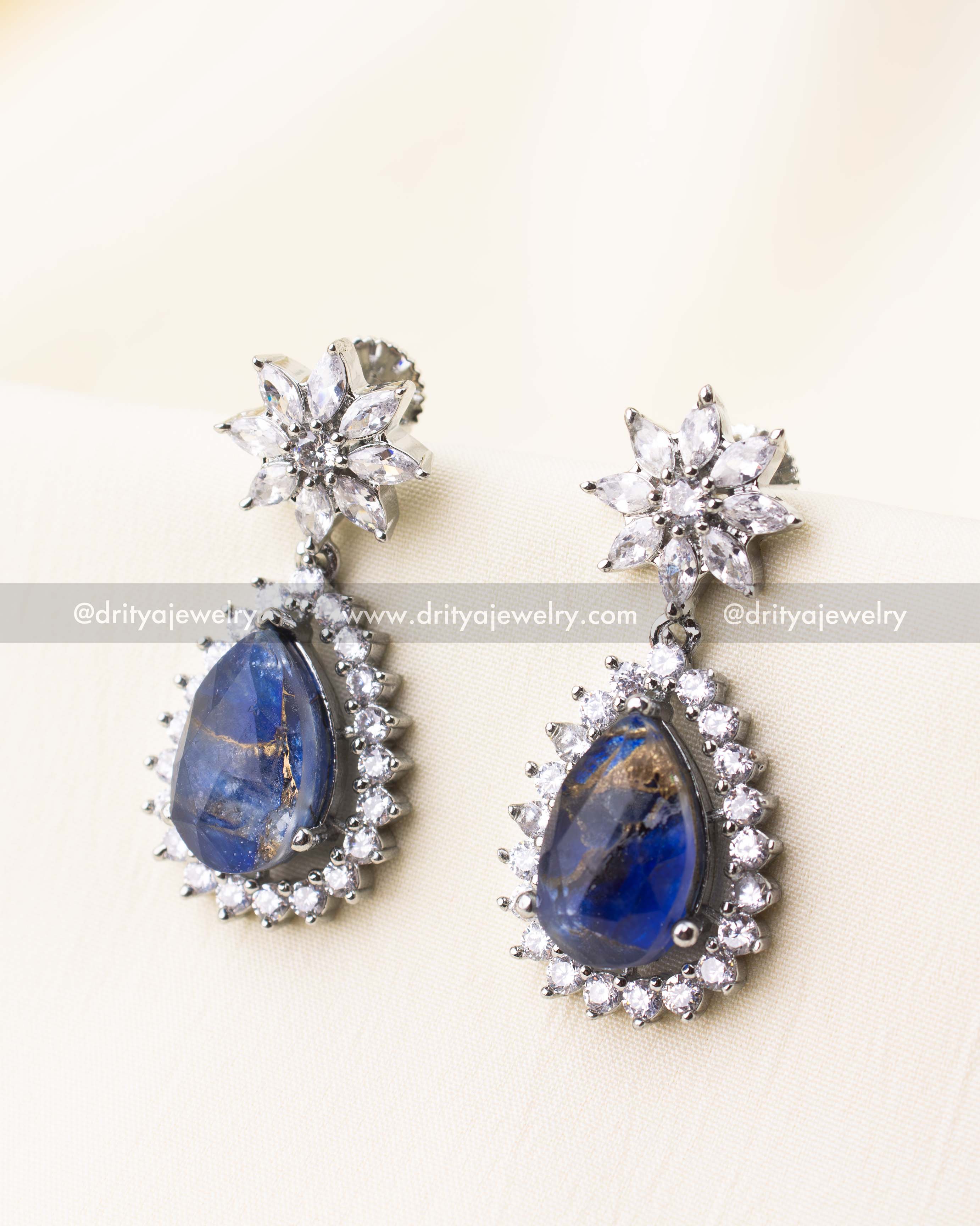 Teardrop earrings with royal blue stones and CZ-studded floral tops in silver finish.