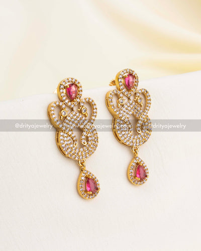 Gold-plated drop earrings with ruby red stones and intricate CZ swirl pattern.