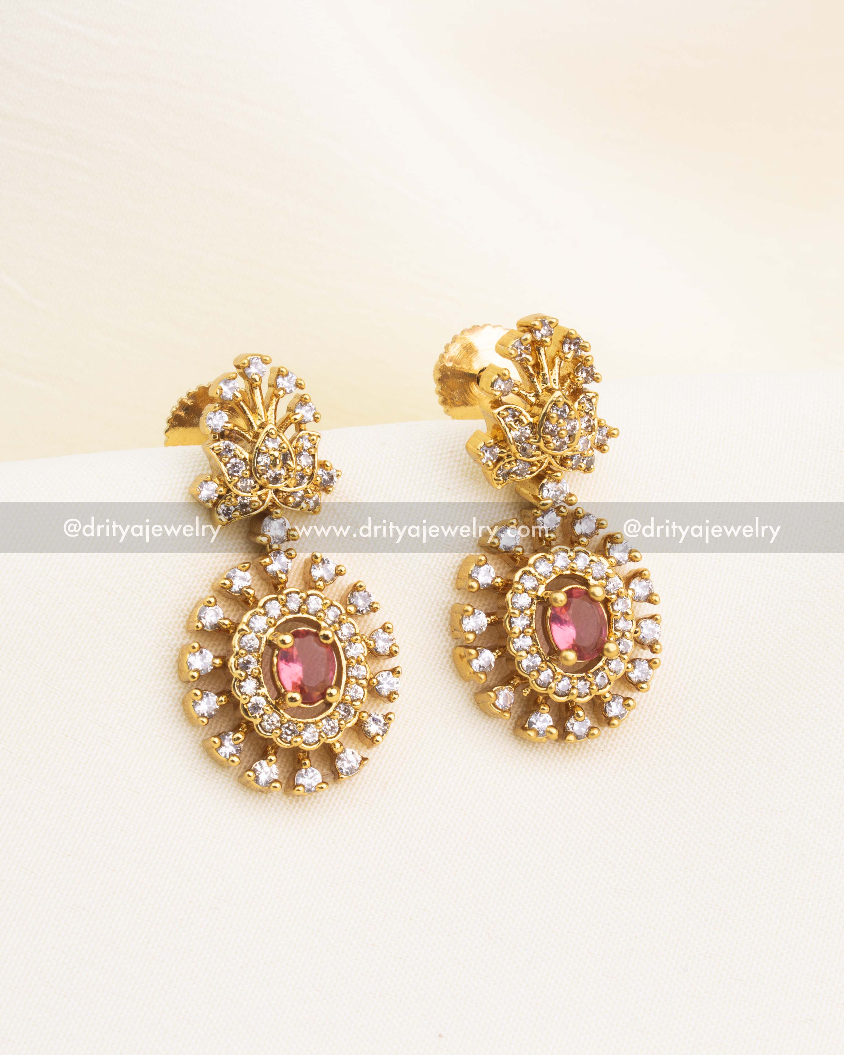 Matching navaratna earrings with red CZ centerpiece and circular halo design in gold finish.