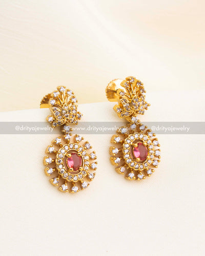 Matching navaratna earrings with red CZ centerpiece and circular halo design in gold finish.