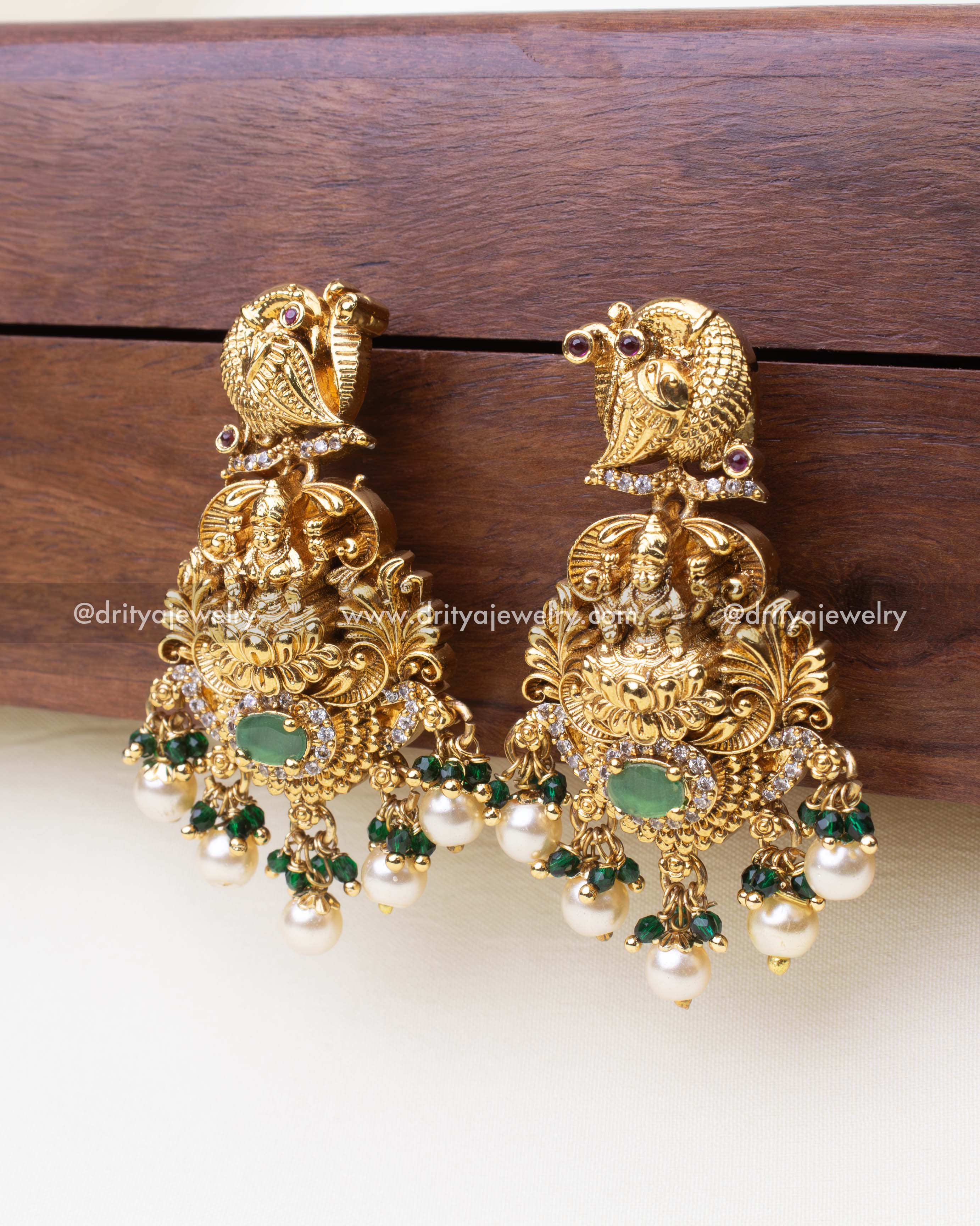 Detailed side view of traditional gold danglers with emerald green and pearl clusters.