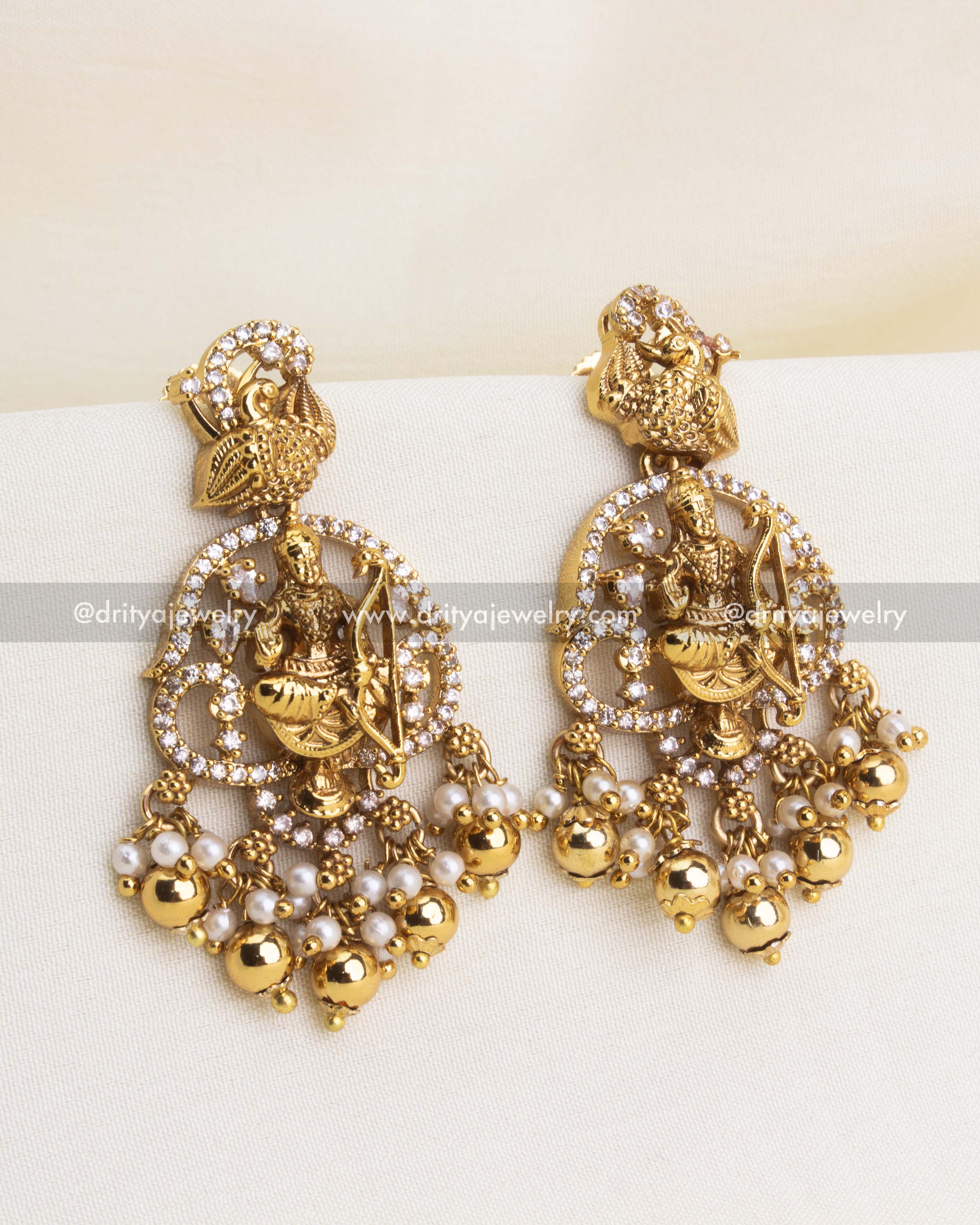 Close-up of matching danglers with deity motifs, peacock detailing, and bead clusters.