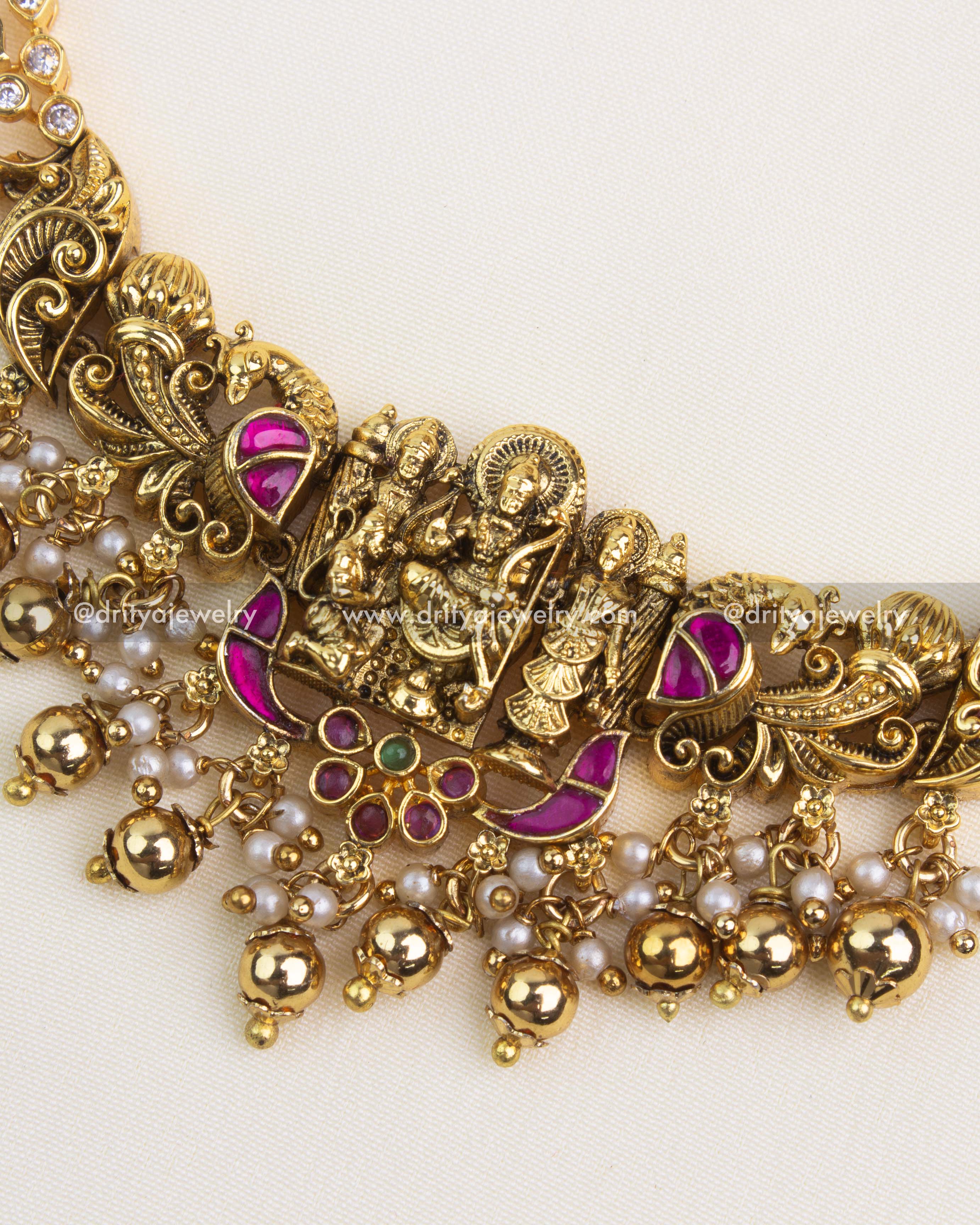 Close-up of nakshi carving with peacock scrolls, ruby–green kemp accents and CZ halos on antique temple necklace.