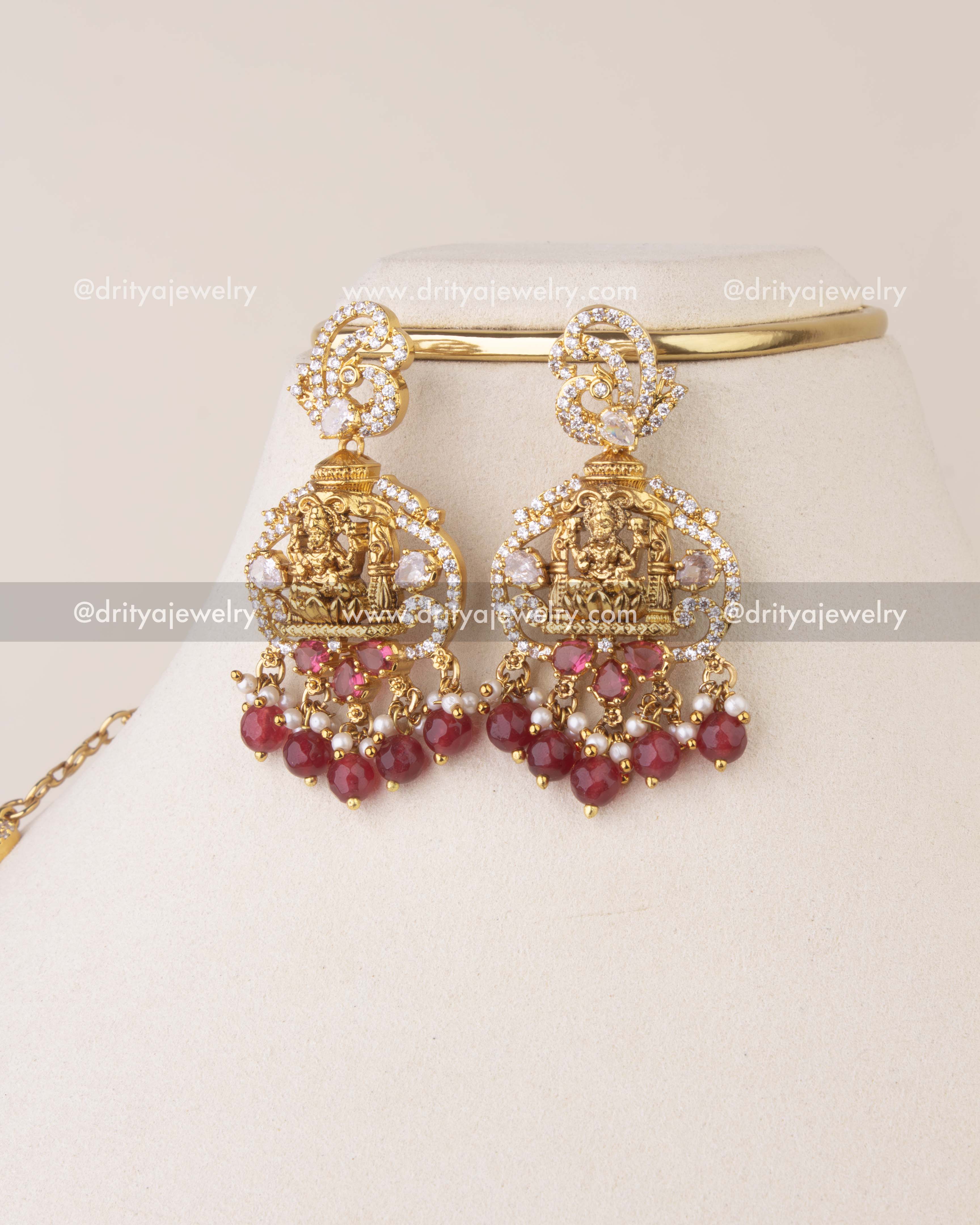 Temple-style earrings featuring Goddess Lakshmi motif with ruby beads and CZ detailing.