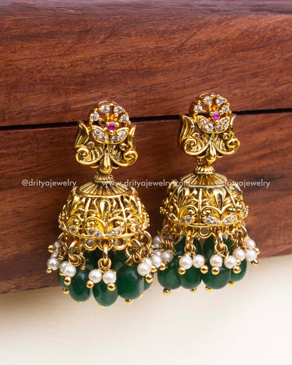 Temple-style jhumka earrings with floral top, antique gold finish, and green bead drops.