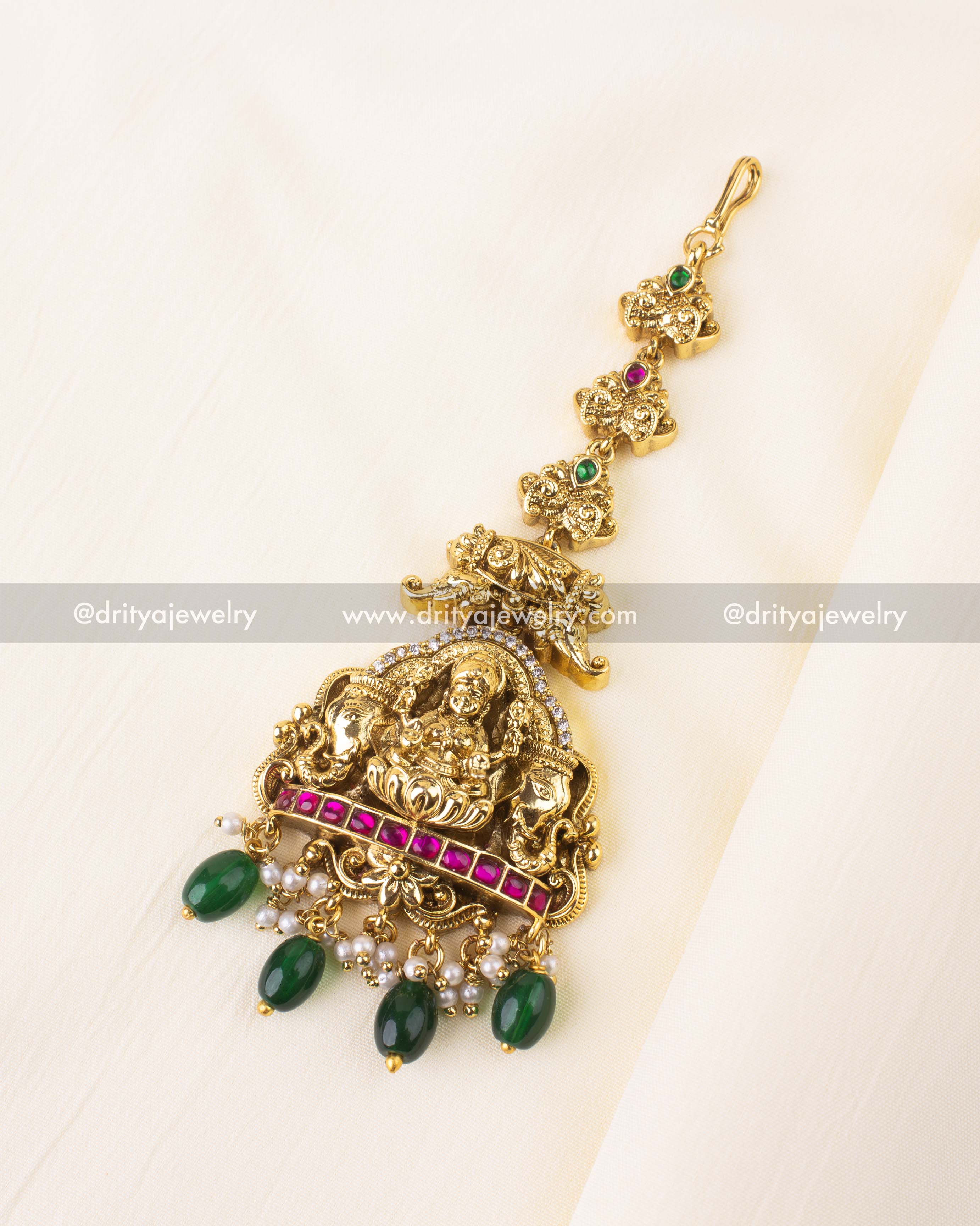 Temple-style maang tikka with Lakshmi Devi motif and emerald green bead drops.