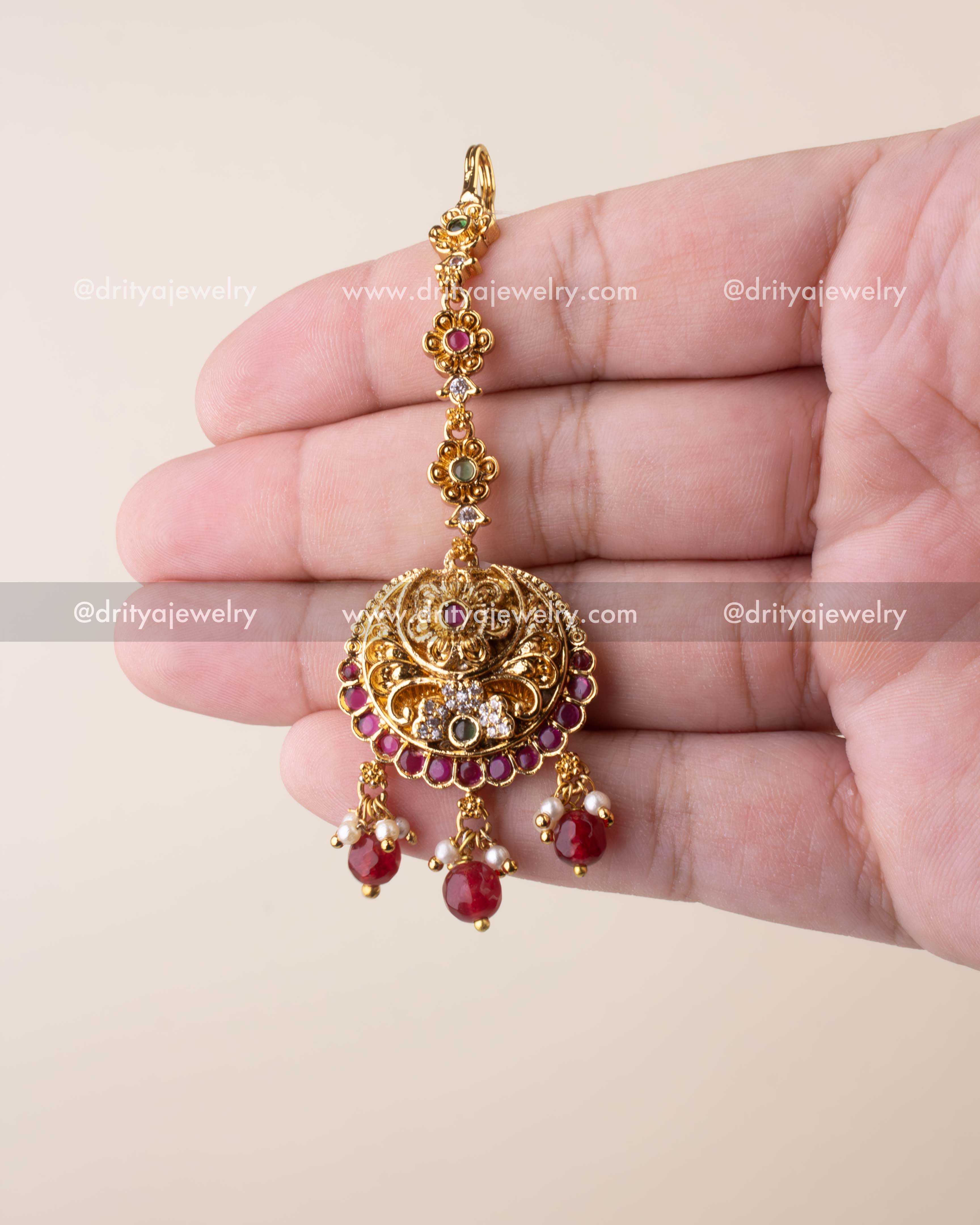 Traditional Nakshi maang tikka with antique gold finish, ruby drops, and pearl embellishments.