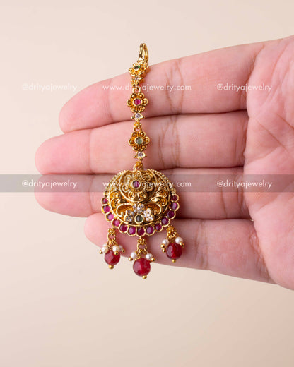 Traditional Nakshi maang tikka with antique gold finish, ruby drops, and pearl embellishments.