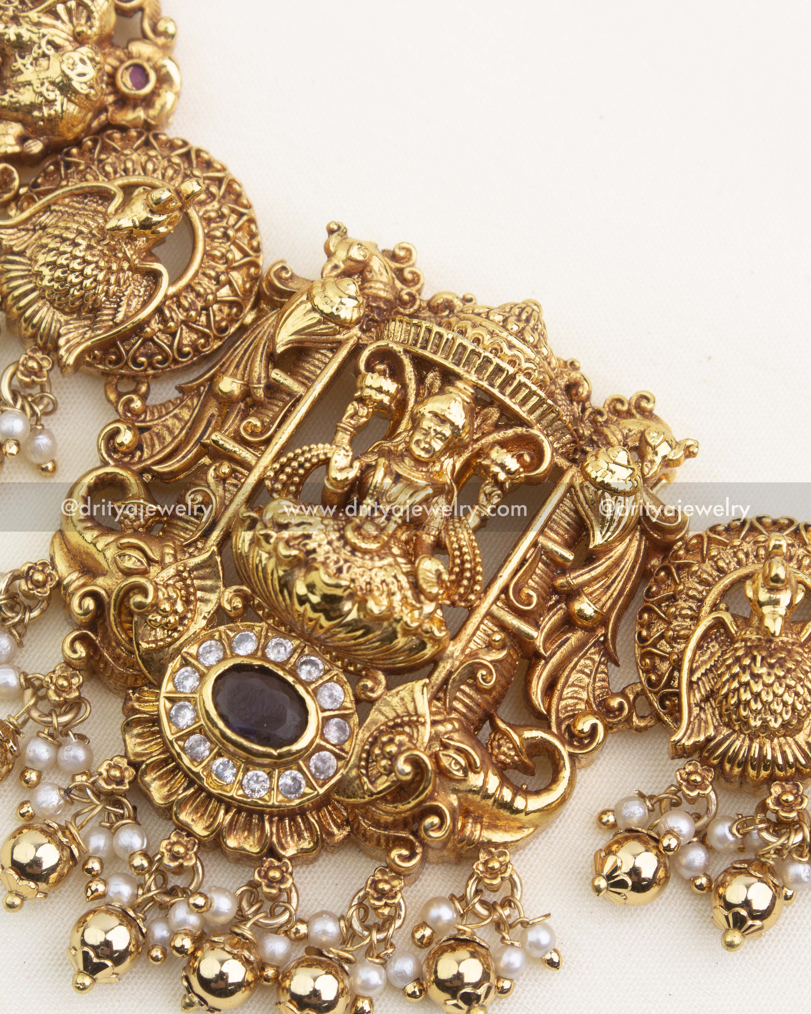 Close-up of temple nakshi centerpiece with goddess carving, CZ framing, peacock elements, and traditional pearl hangings.