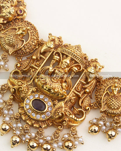 Close-up of temple nakshi centerpiece with goddess carving, CZ framing, peacock elements, and traditional pearl hangings.