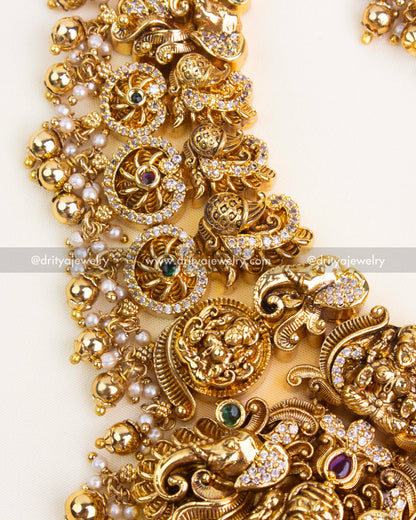 Close-up of nakshi carving with coin medallions, ruby–emerald accents, and micro pavé AD stones on antique gold finish.