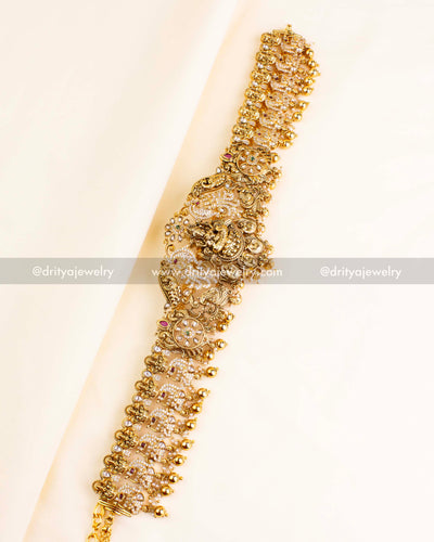 Intricate Nakshi temple waist belt featuring goddess motifs and polki stones with gold bead hangings.