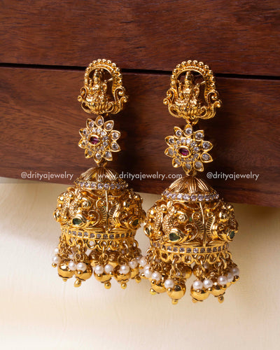 Temple-style gold-plated Jhumka earrings with deity carvings, floral motifs, and pearl embellishments.