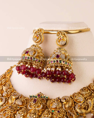 Large Nakshi jhumkas with peacock motifs, ruby bead clusters, and pearl accents.
