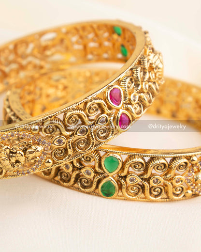 Pair of handcrafted temple bangles with ruby, emerald, and CZ embellishments in antique gold finish.